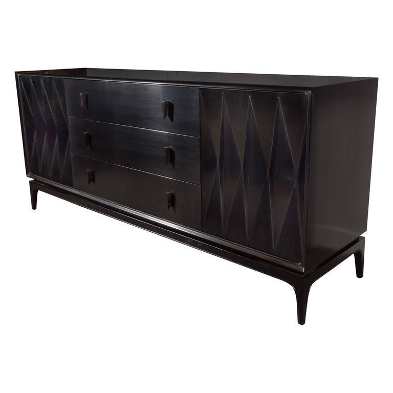 This ebonized walnut sideboard or credenza features two panels with tessellated diamond patterns in relief that open to reveal three interior drawers; gently sloping tapered feet; and three spacious center sliding drawers offering a wealth of