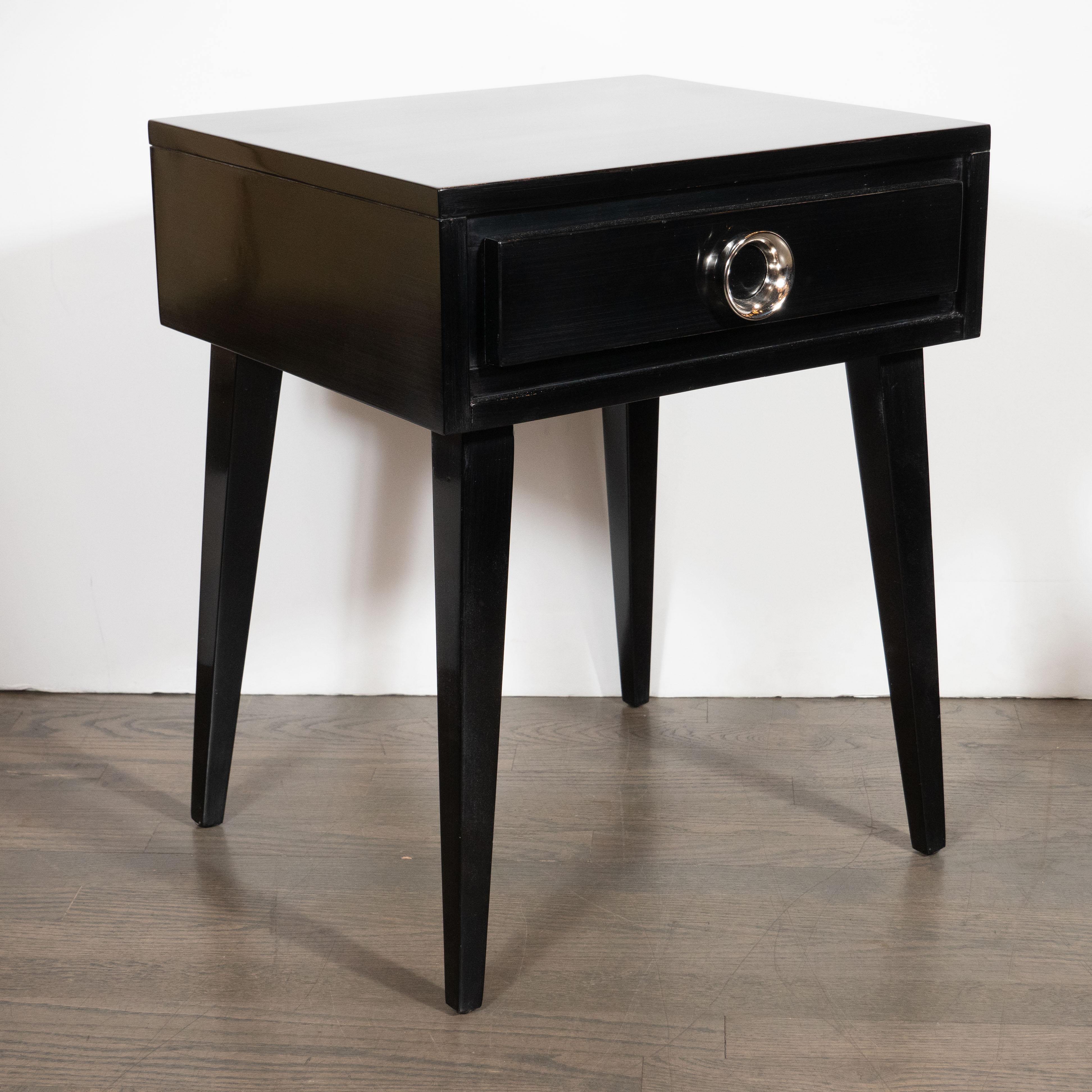 This elegant pair of Mid-Century Modern nightstands were realized in the United States, circa 1950. They features volumetric rectangular bodies with tapered rectangular legs; a central drawer; and circular nickeled pulls. With their clean modernist