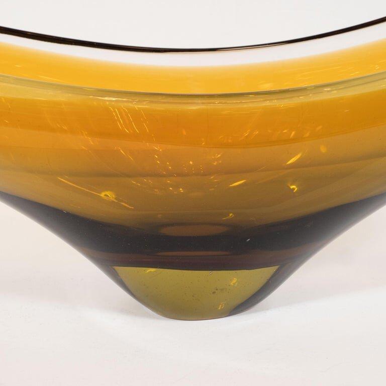 This stunning Mid-Century Modern bowl was hand blown in Murano, Italy, circa 1970. It offers an elliptical form with a concave center realized in a rich amber gradient hue. Sculptural and executed in a refined and versatile palate, this piece would