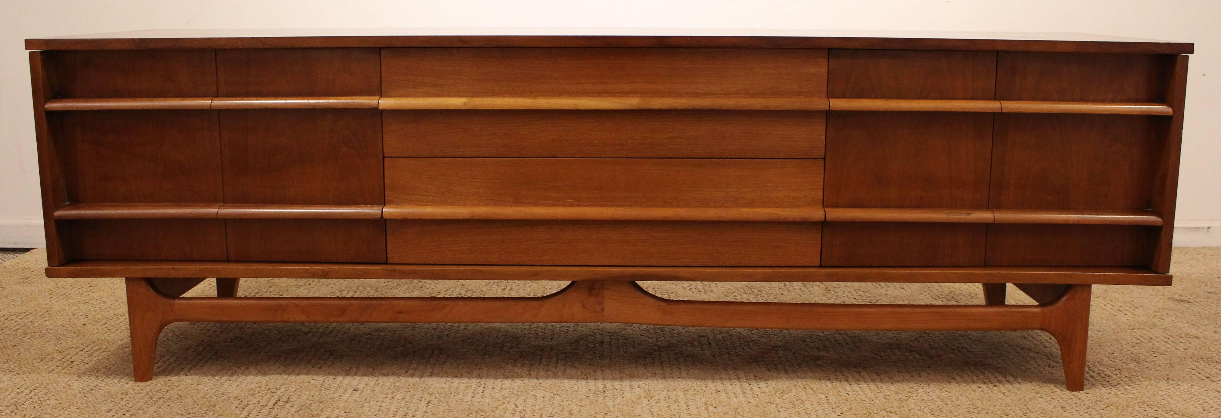 Offered is a beautiful Mid-Century Modern credenza. This piece is made of walnut, featuring a concave front, two bi-folding doors  and three center drawers with sculpted pulls. It is in excellent condition, top has been refinished, showing some age