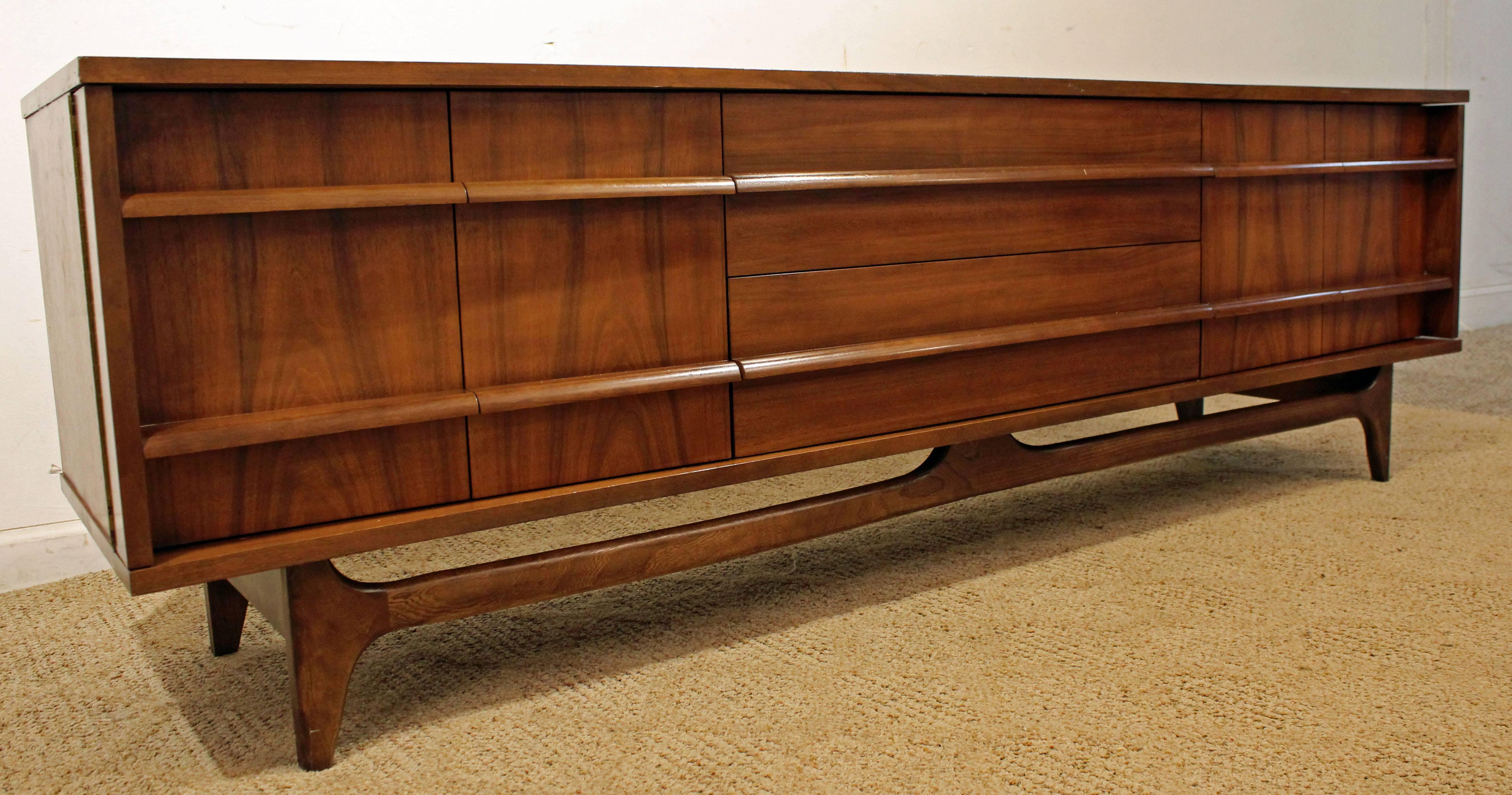 Offered is a beautiful Mid-Century Modern credenza. This piece is made of walnut, featuring a concave front, two doors on both sides and three centre drawers with sculpted pulls. The top has been refinished, shows some age wear. It is signed by
