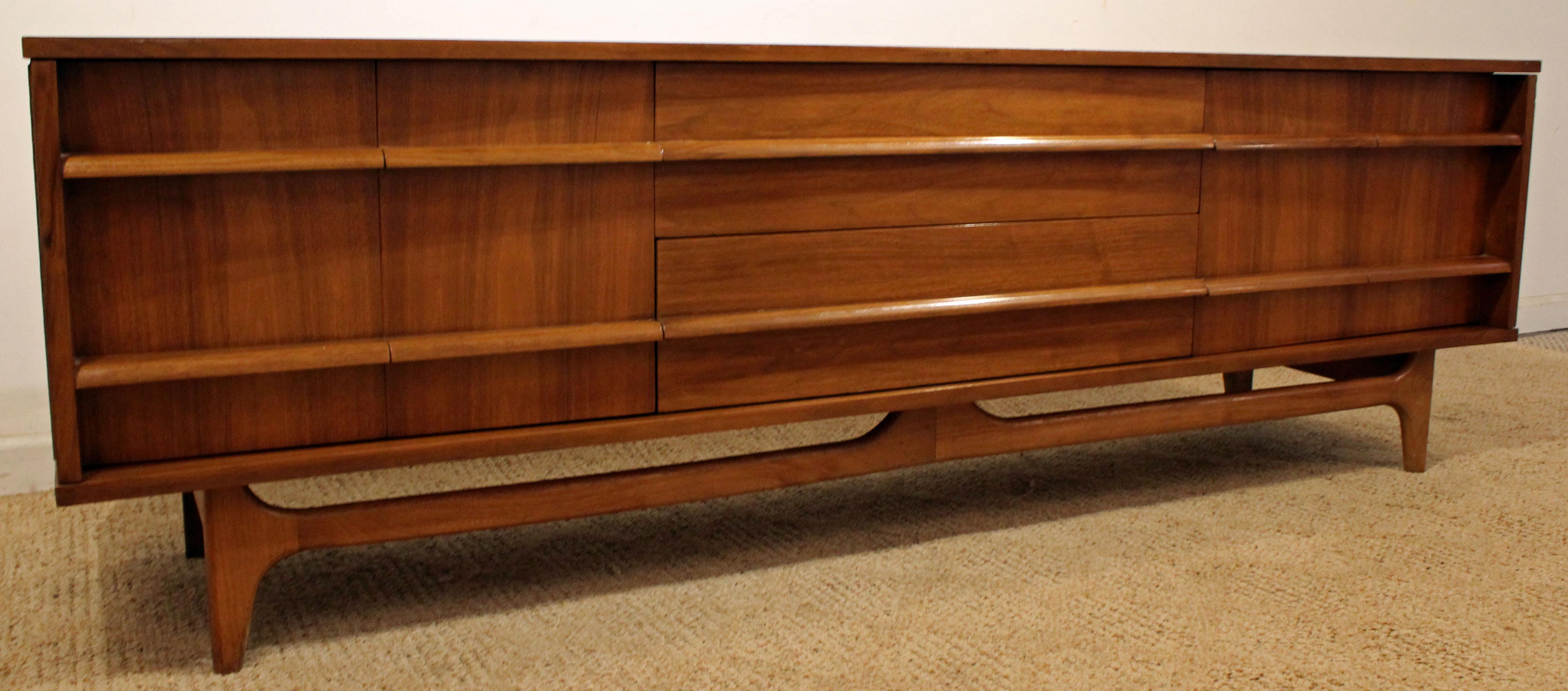 Offered is a beautiful Mid-Century Modern credenza. This piece is made of walnut, featuring a concave front, two doors on both sides and three centre drawers with sculpted pulls. The top has been refinished, shows minor age wear. It is signed by