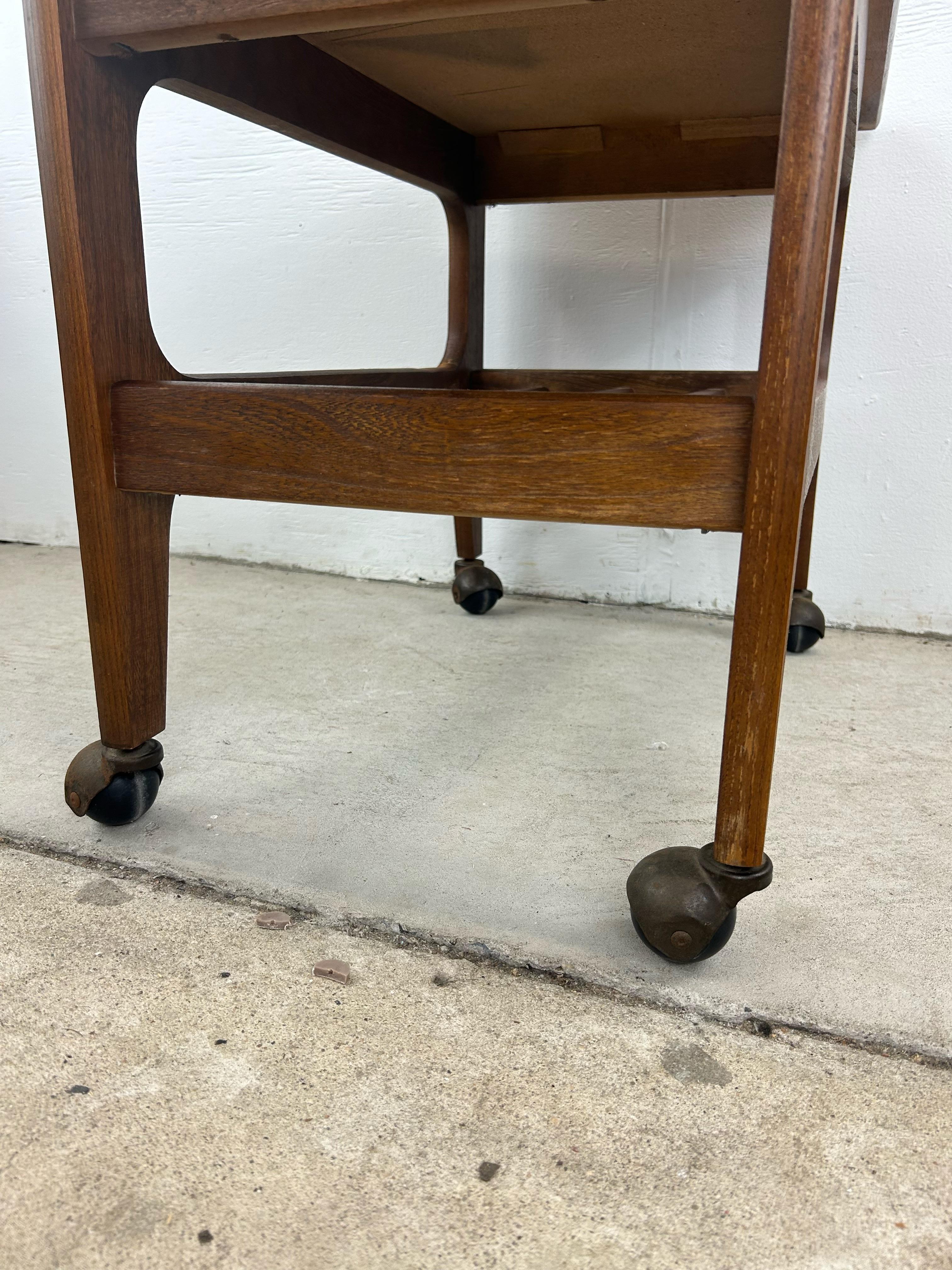Esta mesa de centro moderna de mediados de siglo está fabricada en madera dura, tiene un resistente tablero lacado en negro, un estante de tablillas debajo y ruedas giratorias de latón.
u2028Dimensiones: 26.5w 16d 20h 

Estado:  El acabado original