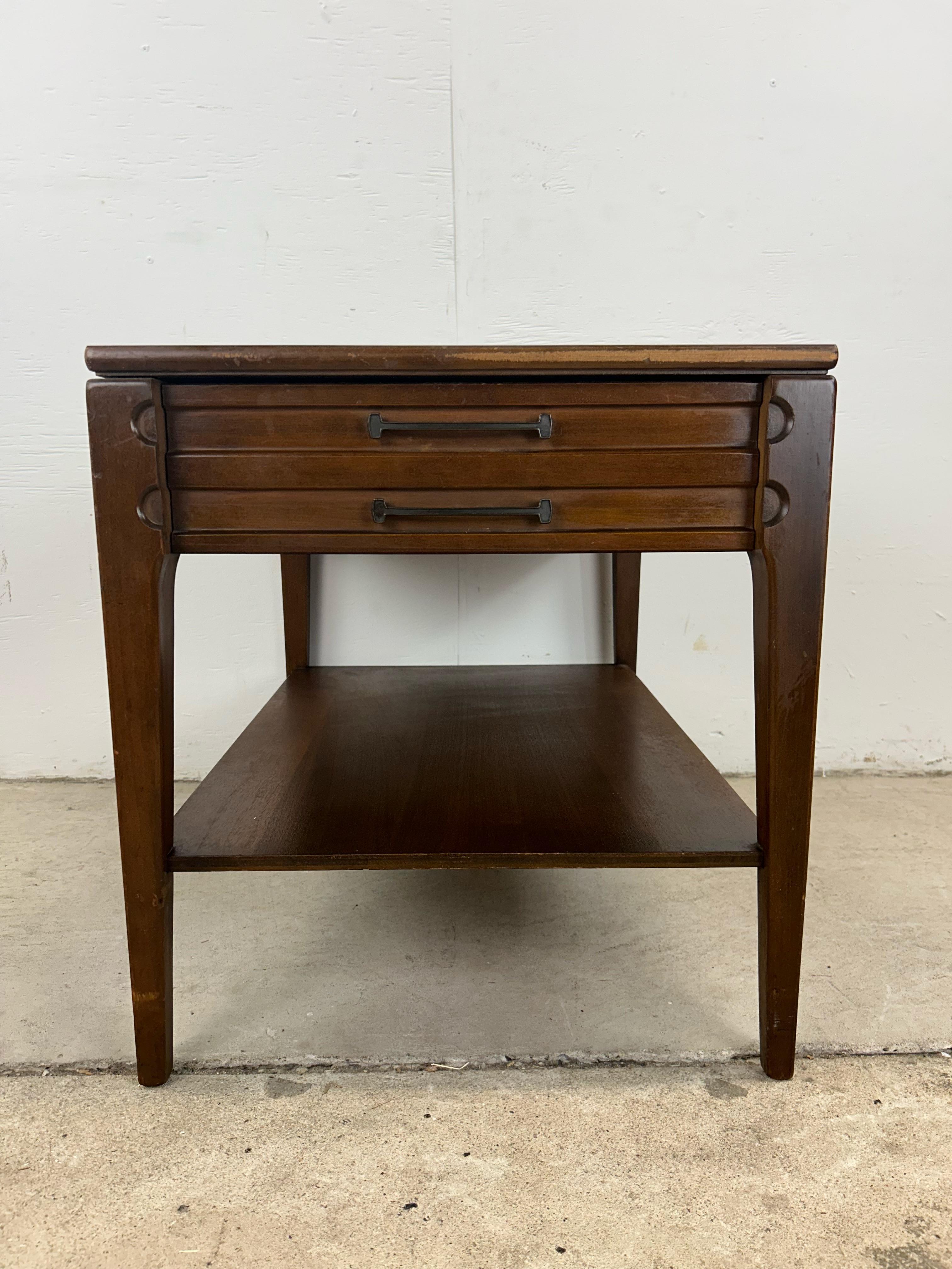This mid century modern end table by Mersman features hardwood construction, single dovetail drawer, tall tapered legs, open storage shelf, and durable vinyl top with faux wood grain.
 Dimensions: 19.5w 27.5d 21.25h

Condition: Original finish is in