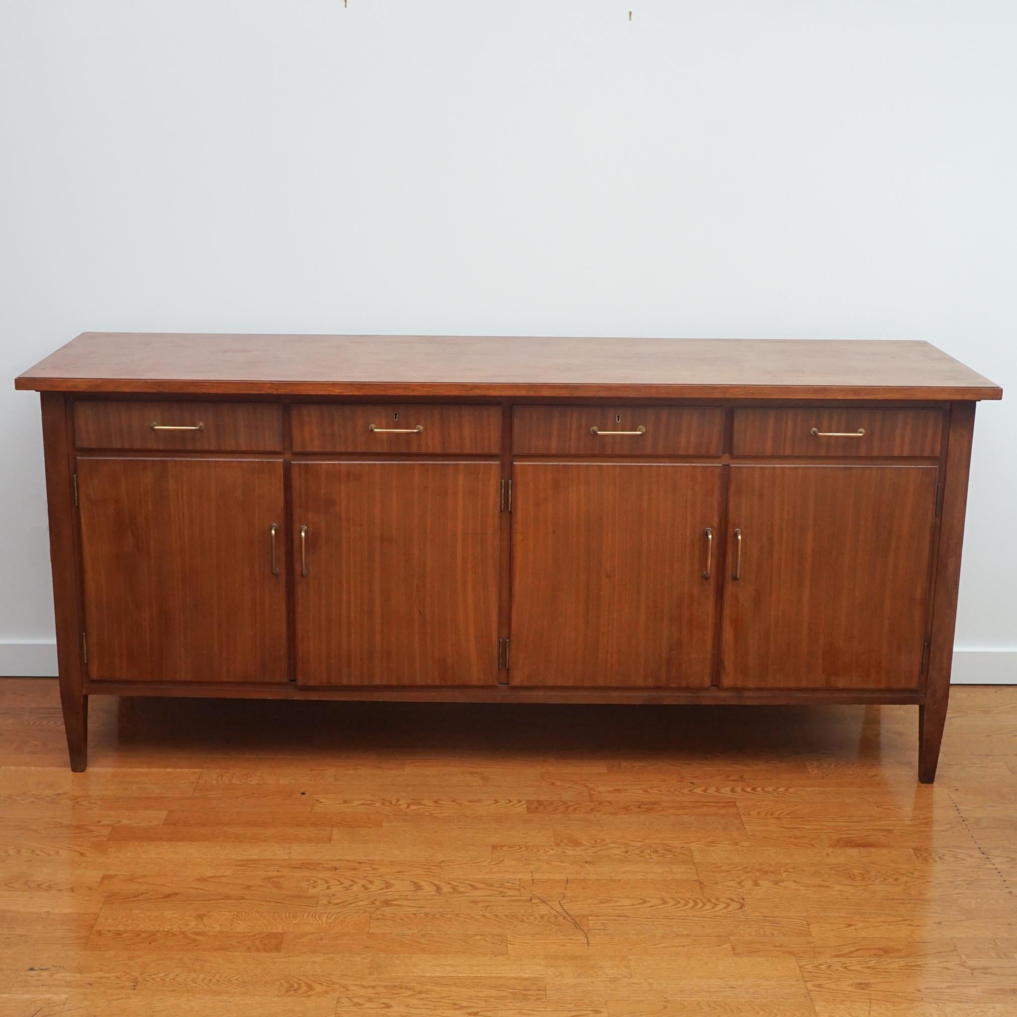 The rich wood tone and classic lines of this English sideboard from the 1960s makes it a highly desirable piece today. Featuring four cabinet doors and four top drawers, the sideboard can be used anywhere decorative storage is needed—dining room,