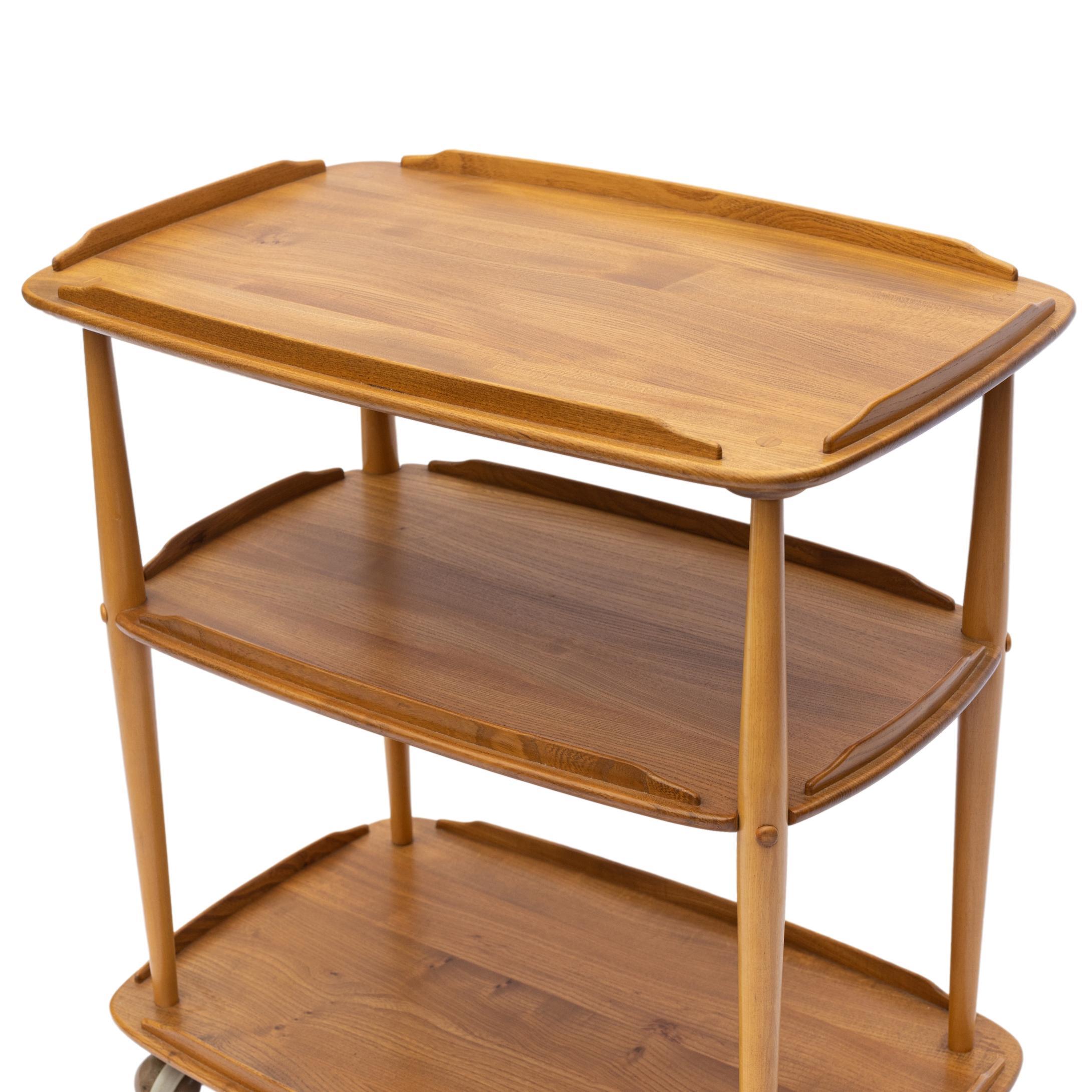 Mid-Century Modern ERCOL Elm and Beech Bar Trolley Designed by LUCIAN ERCOLANI, with three solid elm tiers with molded galleries, the beech posts with tenon and mortised joinery, on brass castors, English, ca. 1955 
Ercol was founded in 1920 by the