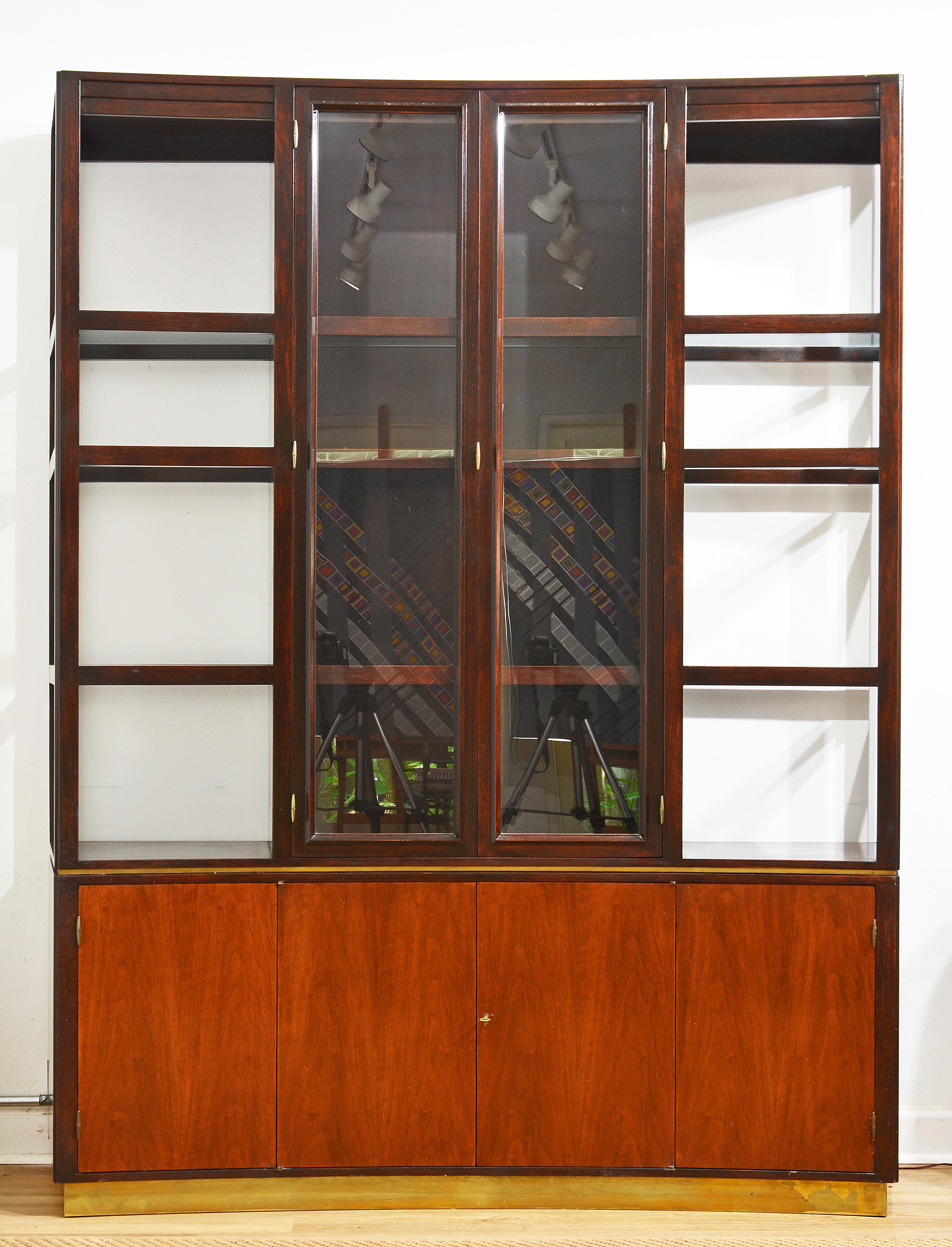Designed by Edward Wormley with a 'Less is More' aestethic this walnut wallunit offers three shelved cabinets under three tier glass shelving incorporating a center display cabinet with glazed doors. The front of the unit is slightly concave adding