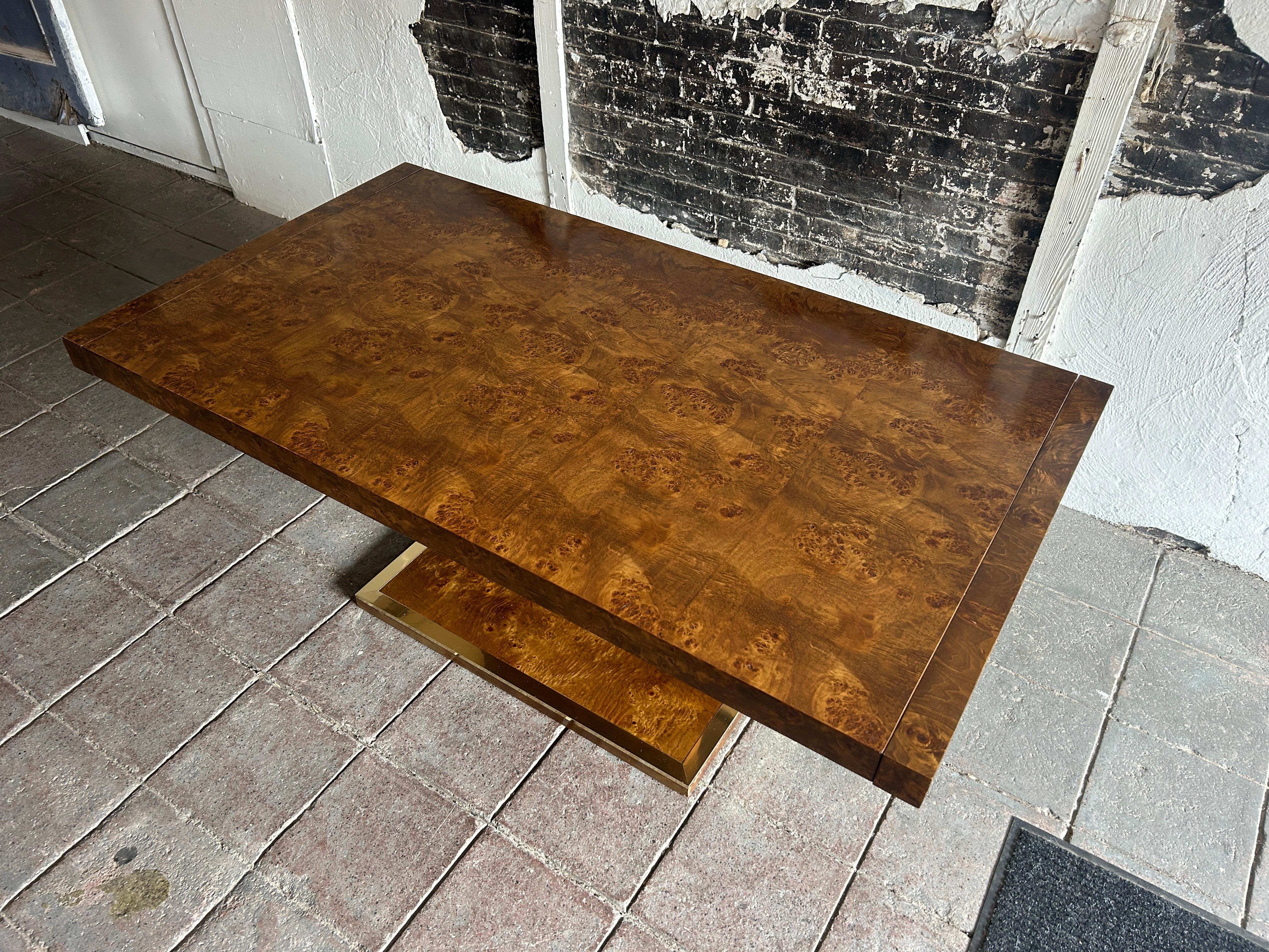 Mid century modern dining table attributed to  Milo Baughman / Thayer Coggin. The dining table sits on a center burl wood base with brass accents. The 3” thick top is patchwork burl veneer wood with a medium brown finish. Table has (2) leaves that