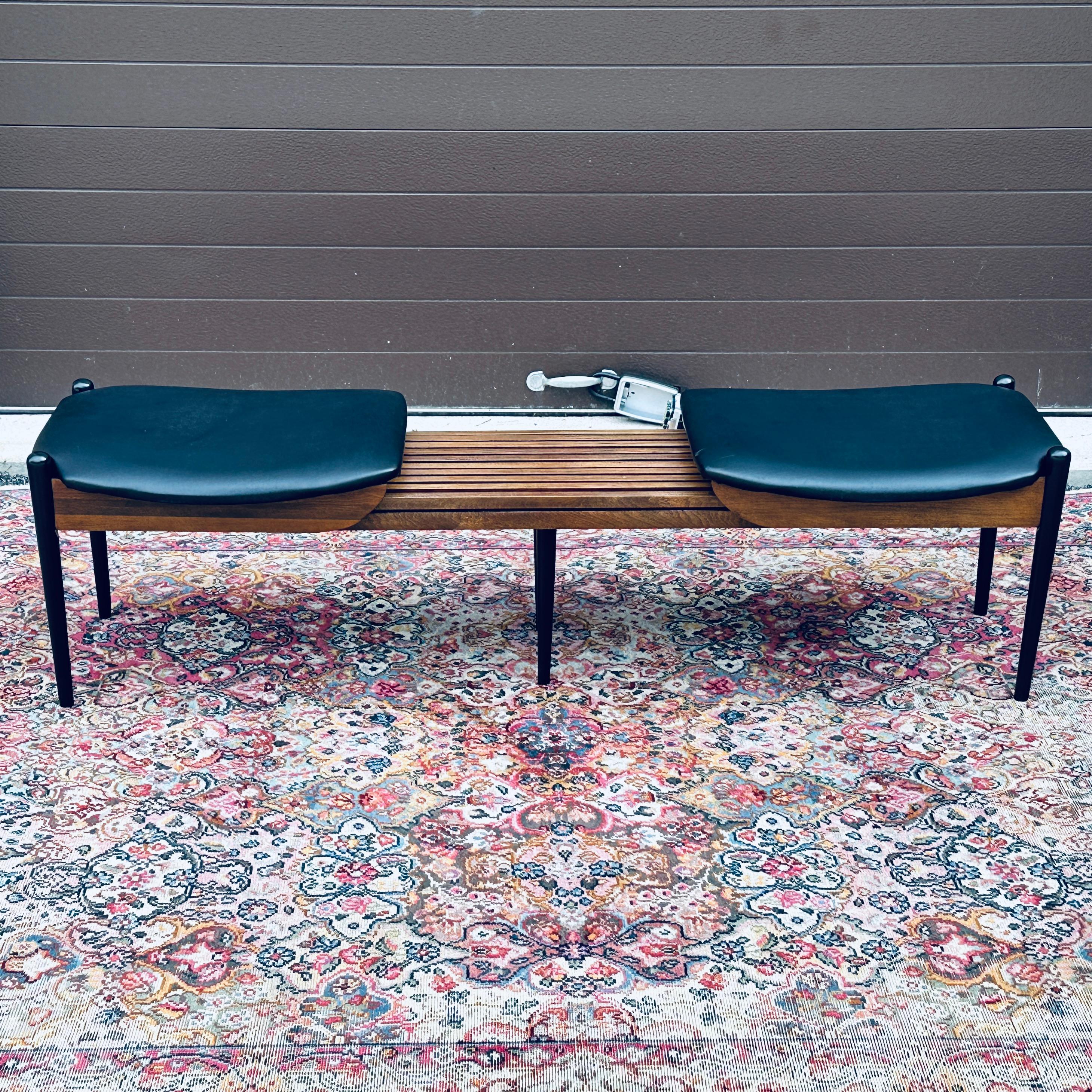 An amazing mid-century modern wooden bench on black pencil legs with two shaped upholstered seats circa 1960. This bench expands creating a slatted center table area. Designer or maker unknown but often attributed to Arthur Umanoff and John Stuart.