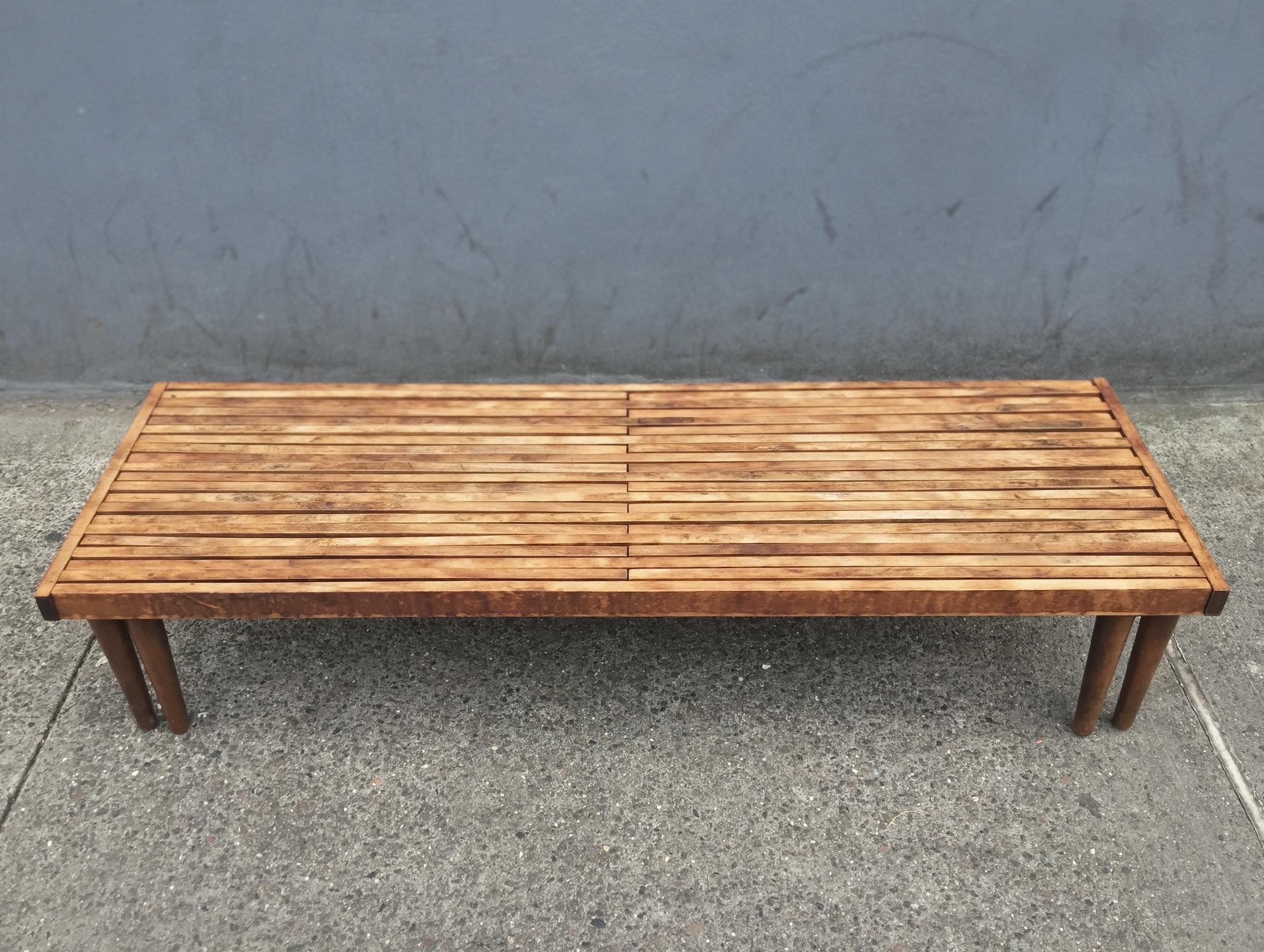 A handsome honey-toned slatted bench designed by John Keal for Brown Saltman in the 1960s. It is comprised of solid wood and reinforced by steel on the underside. The design of the bench allows for the slats to interlock and extend outward on either