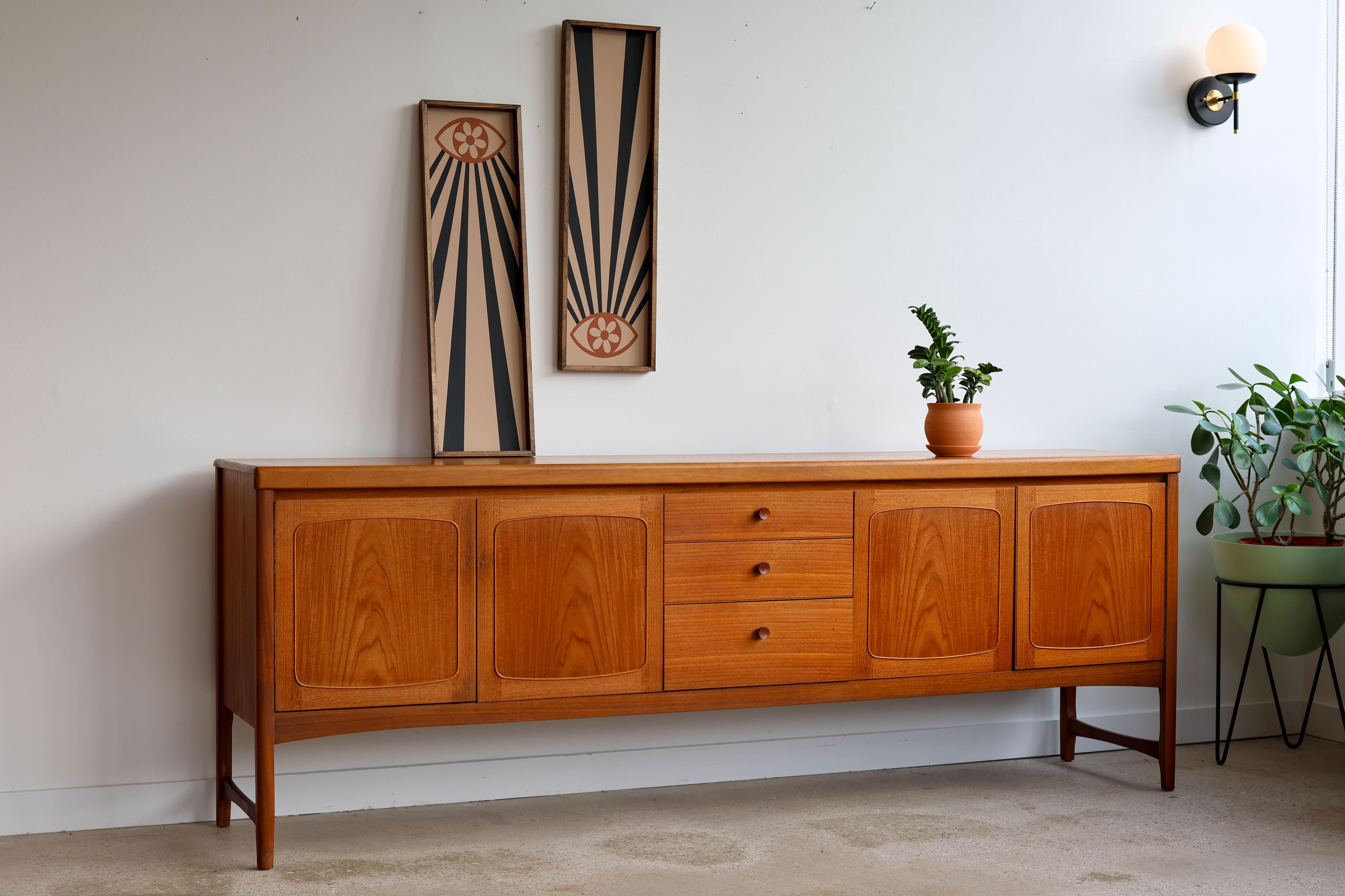 Mid-Century Modern teakwood credenza.
Teak sideboard by Nathan Furniture, UK, 1960s. 
Symmetrical sideboard with two sets of double cabinets and shelves.
Three dovetailed drawers; top drawer holds dividers.
Excellent vintage condition.

84” long x