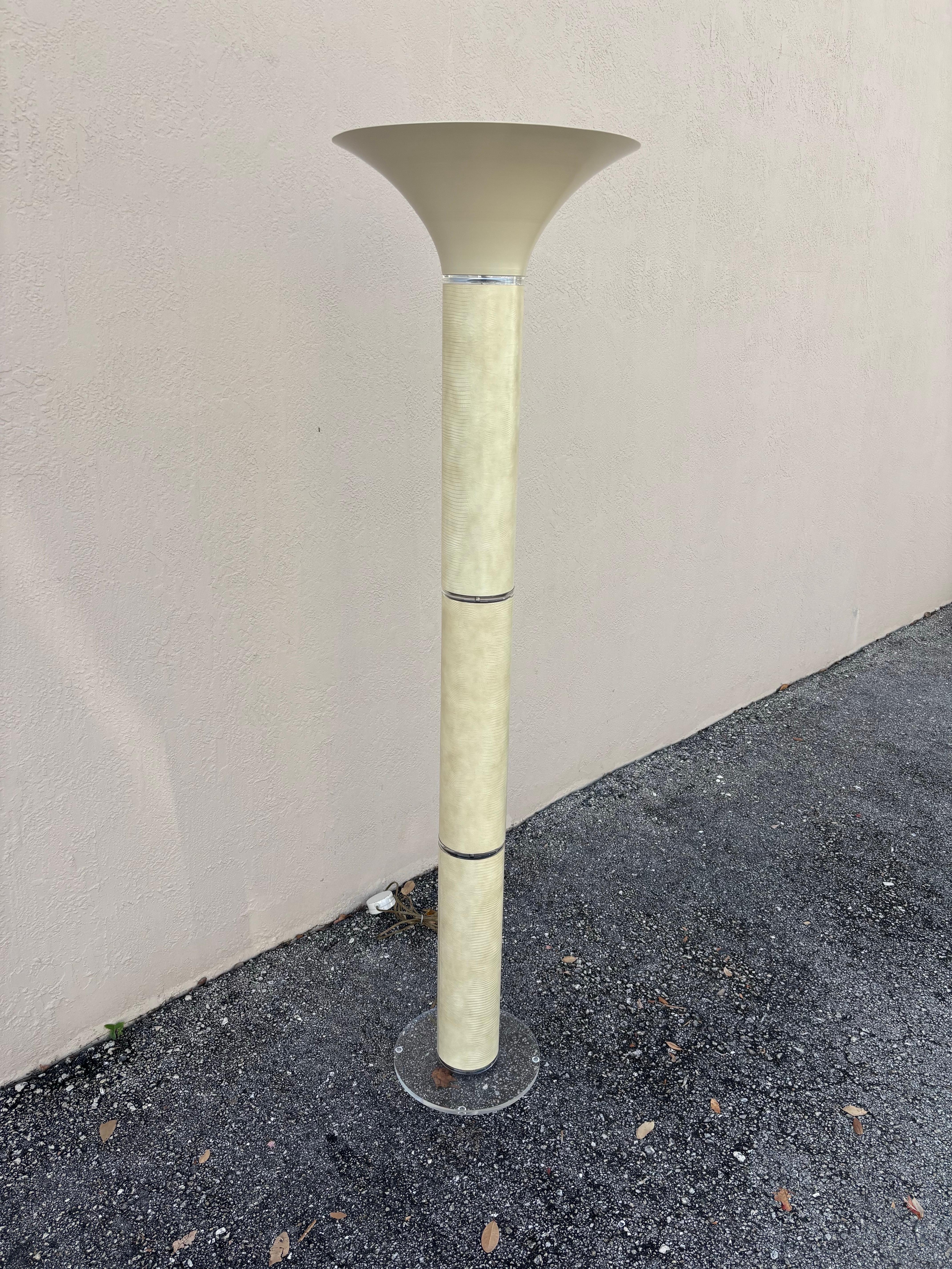 Lámpara de pie fabricada por Optique. Una pantalla de antorcha metálica sobre un largo cuerpo cilíndrico recubierto de piel de cocodrilo repujada. Detalles de lucita y base de lucita. Con cable y accionamiento por pedal. Un bonito color arena
