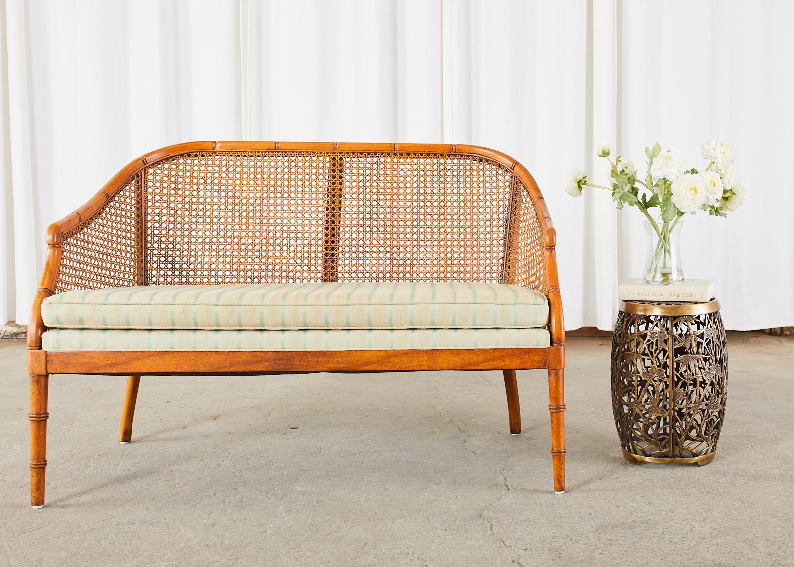 Charming mid-century settee or loveseat featuring a faux-bamboo carved frame. The frame is inset with cane having a gracefully curved back ending with scrolled arms. The seat has a loose seat cushion with vintage fabric. Excellent joinery and