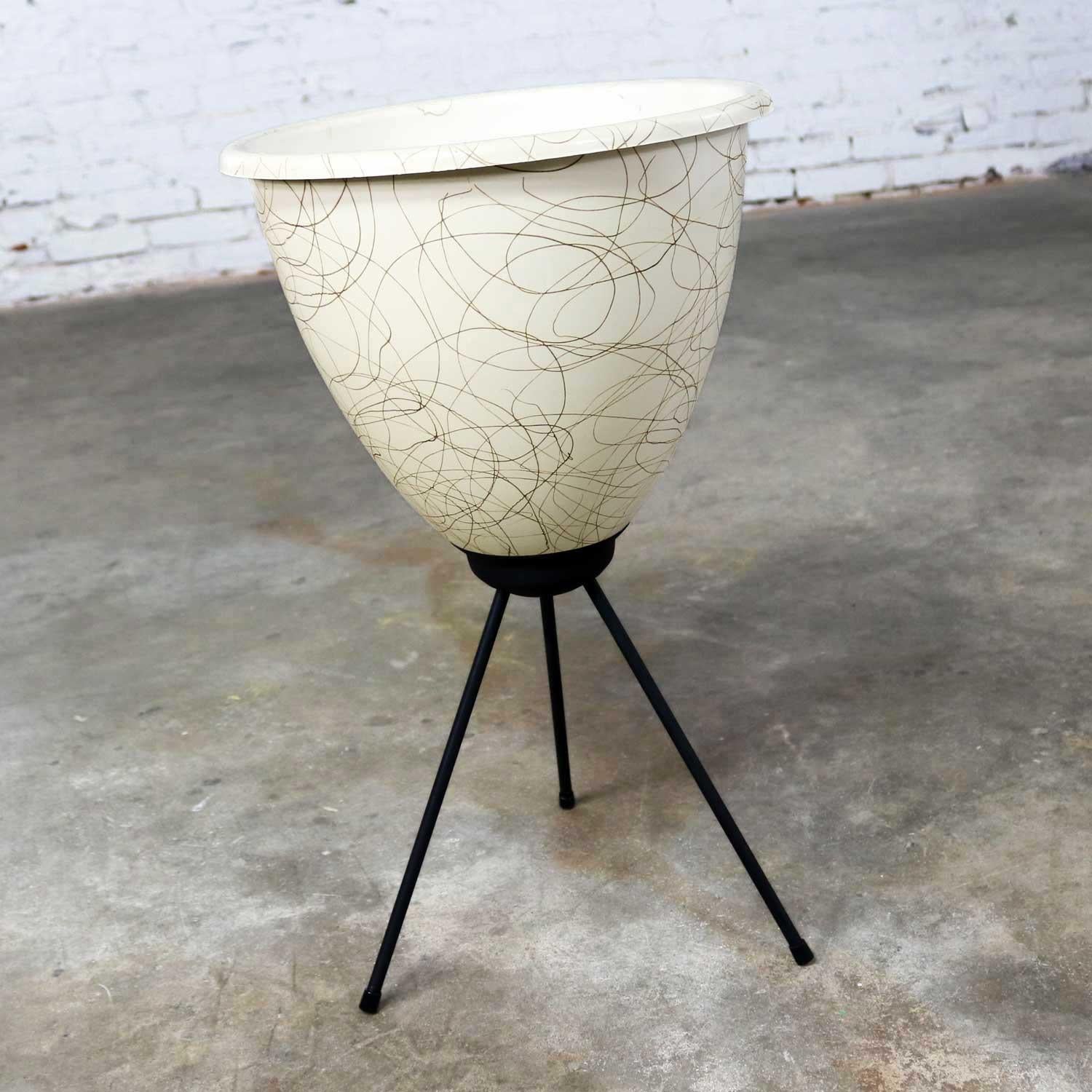 Handsome Mid-Century Modern bullet planter in eggshell white and gold swirled fiberglass with a lip around the edge and an attached black iron set of tripod legs. This planter is in wonderful vintage condition overall. There are tiny cracks in the