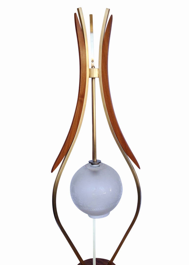 Unique Mid-Century floor lamp with wood base and brass arms. The lamp features an almost free-floating center globe held up by three arms each decorated with rounded hourglass shapes in brass and wood, very reminiscent of the lamps made by Adrian