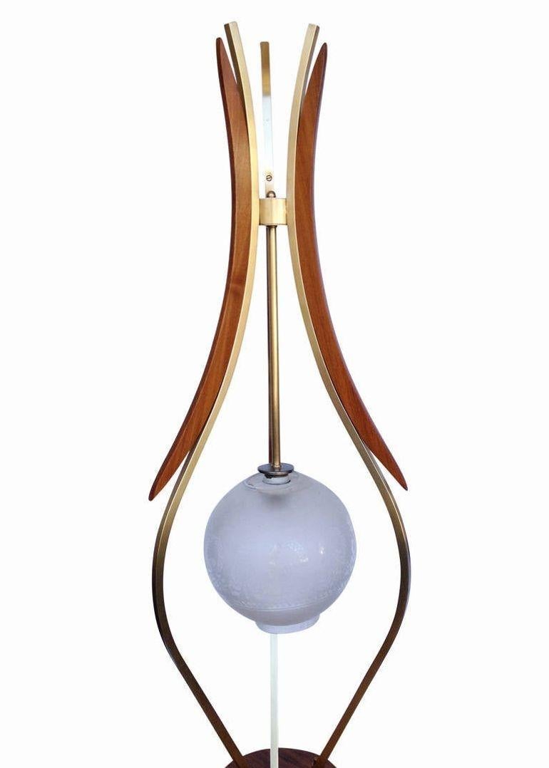 Lámpara de pie única de mediados de siglo con base de madera y brazos de latón. La lámpara tiene un globo central que flota casi libremente, sostenido por tres brazos decorados con formas redondeadas de reloj de arena en latón y madera, que