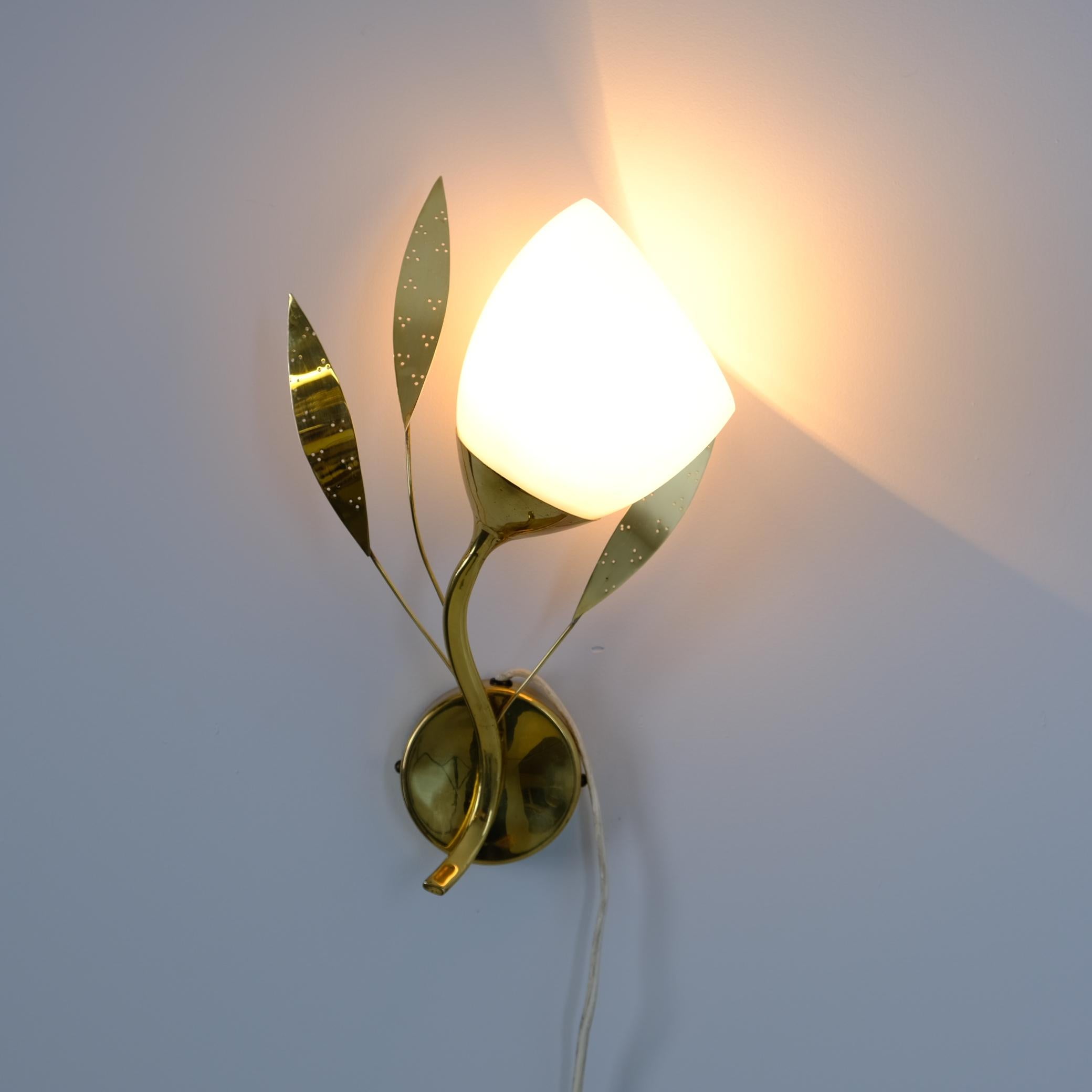 Applique florale moderne du milieu du siècle, modèle EY 35 par Itsu, datant des années 1950. La lampe présente une base ronde avec un bras en forme de Branch et trois feuilles de laiton perforées. L'abat-jour en verre opalin blanc imite une fleur