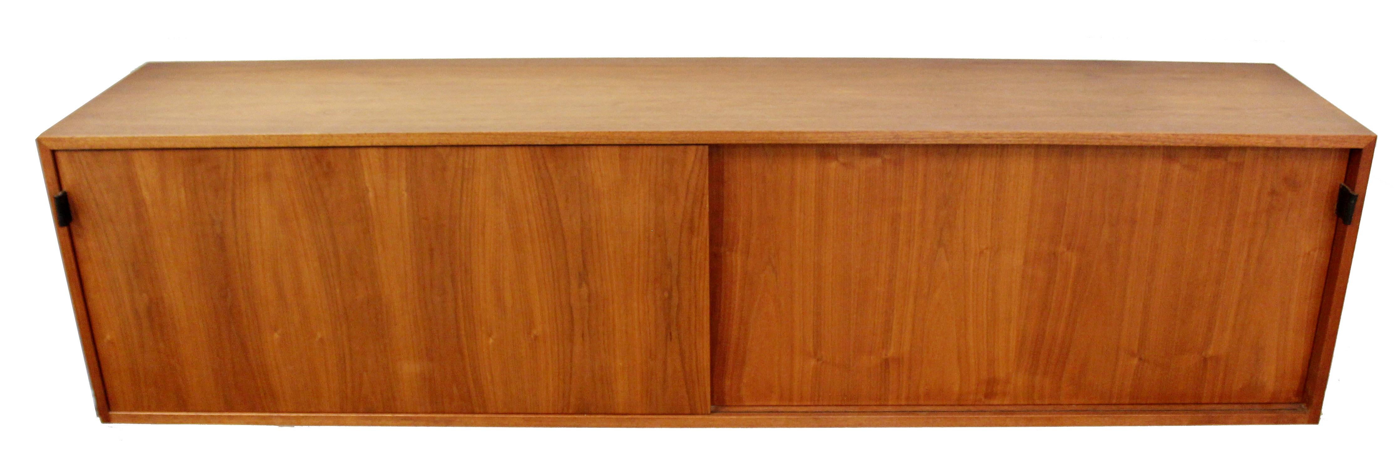 For your consideration is an incredible, floating credenza wall-mounted credenza in walnut wood with sliding doors that reveal four shelves and three drawers, by Knoll, circa the 1960s. Has the original vintage Knoll tag. In excellent condition. The