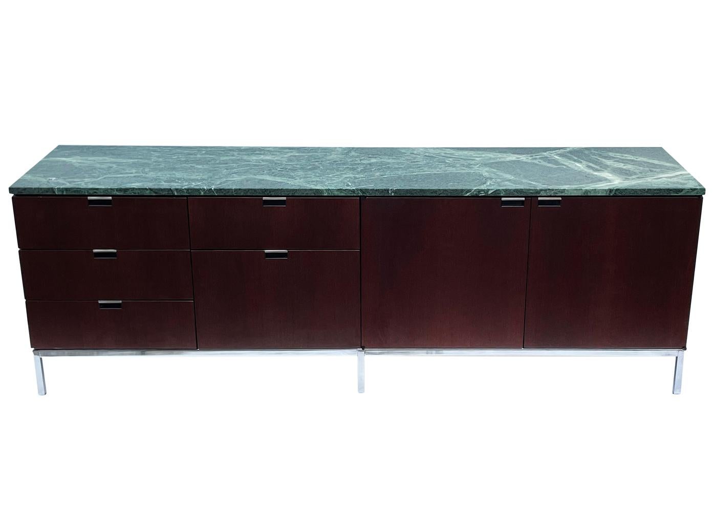 A sleek modern classic cabinet designed by Florence Knoll and produced by Knoll. It features a dark mahogany case, stainless steel legs and a green marble top. We currently have two matching credenzas in stock and they're priced each.