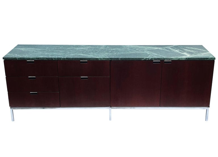 A sleek modern classic cabinet designed by Florence Knoll and produced by Knoll. It features a dark mahogany case, stainless steel legs and a green marble top. We currently have two matching credenzas in stock and they're priced each.