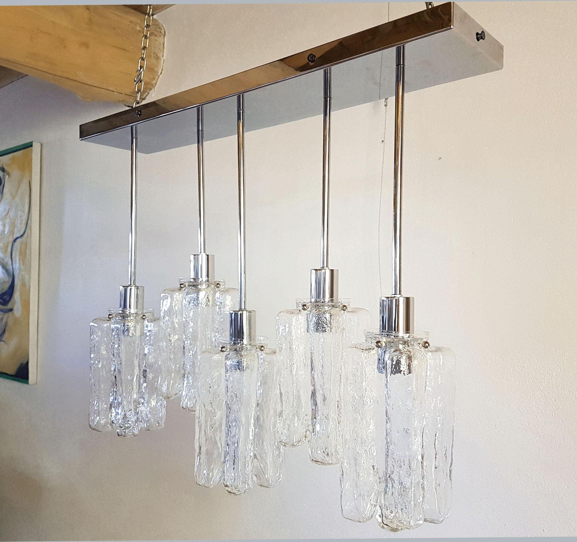 Elongated flush mount chandelier attributed to Kalmar, Italy and Austria 1980s.
The Mid-Century Modern Italian chandelier is made of a rectangular chrome base and 5 clear Murano glass pendants in two heights.
Each Kalmar Murano glass is nesting a