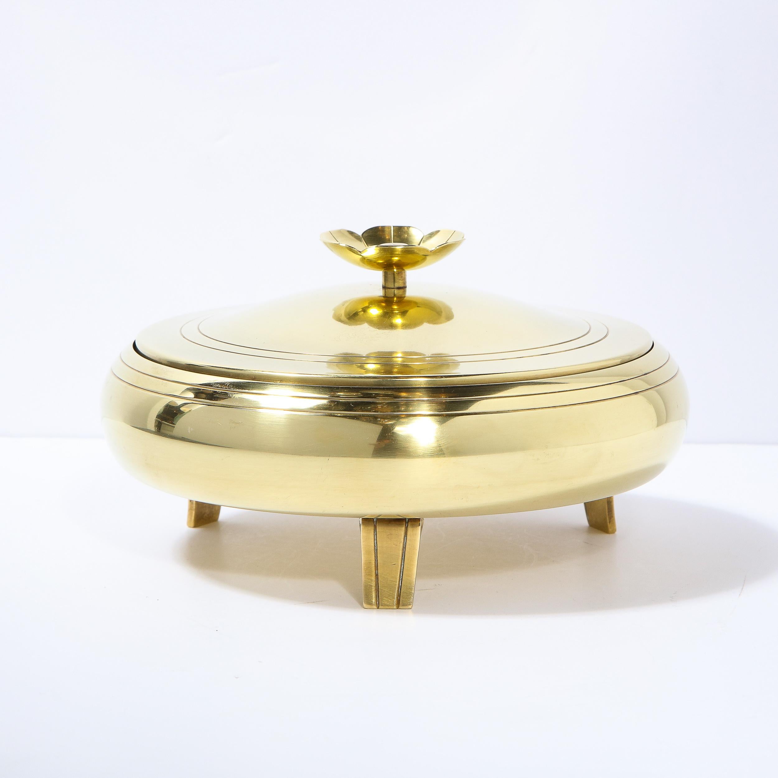 This elegant Mid-Century Modern polished brass bowl was designed by Tommi Parzinger for Dorlyn Silversmiths in the United States circa 1960. It features a circular body with banding detail around the perimeter and a matching lid (also banded) that