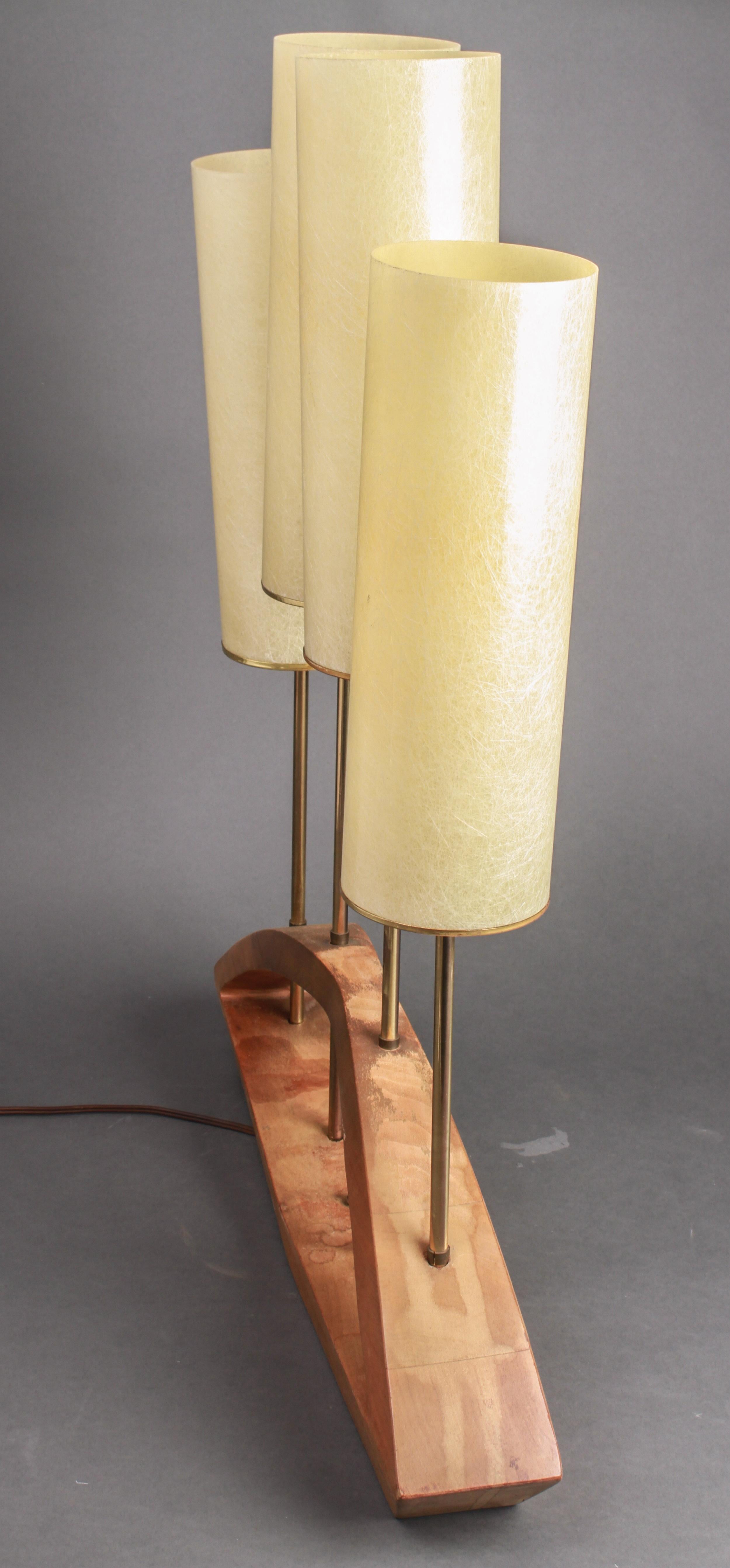 Mid-Century Modern four-light wooden candelabra manner table lamp. The piece has an arched form pierced by four vertical brass standards, each with a tall resin cylindrical shade. In great vintage condition with age-appropriate wear.