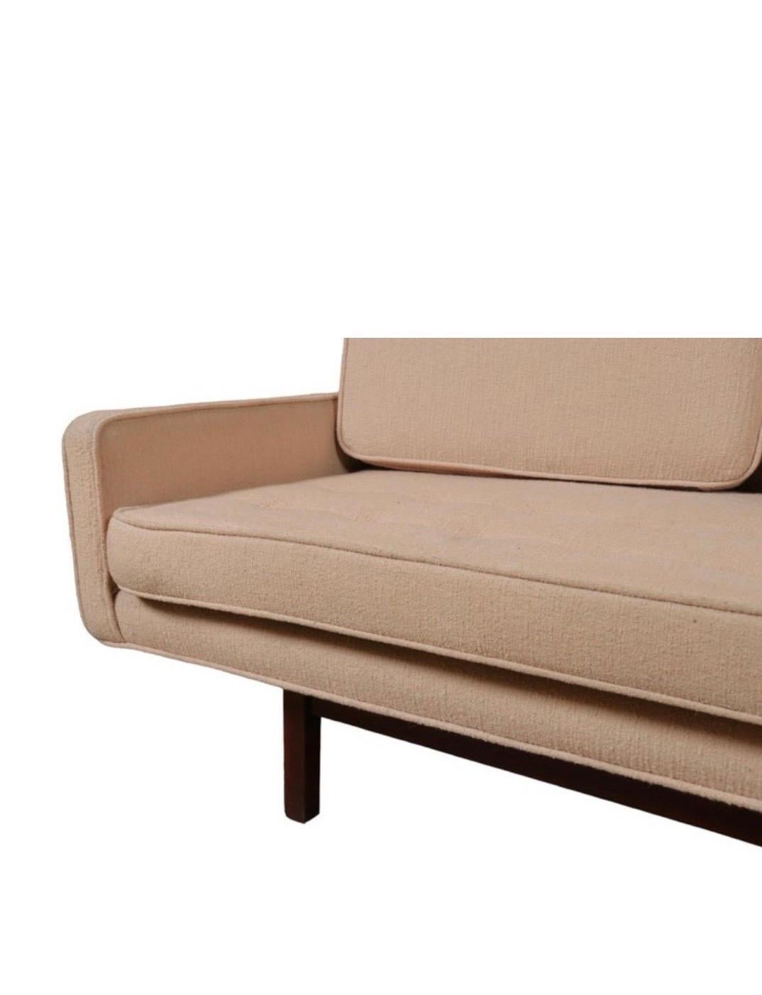 Un raffinato divano a quattro posti con imbottitura in bouclé beige su base tinta scura con gambe quadrate.  Nello stile di Edward Wormley / Dunbar.

USA, circa 1950. Senza segno. Rivestito in un secondo momento.

La tappezzeria presenta segni di