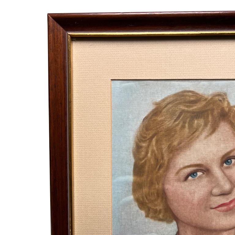 A mid-century modern portrait painting of a woman on blue silk. This portrait is professionally framed in a rectangular wood frame with gilt gold detail. The painting is of a woman in a pink button-up top with short blond hair on a blue background.