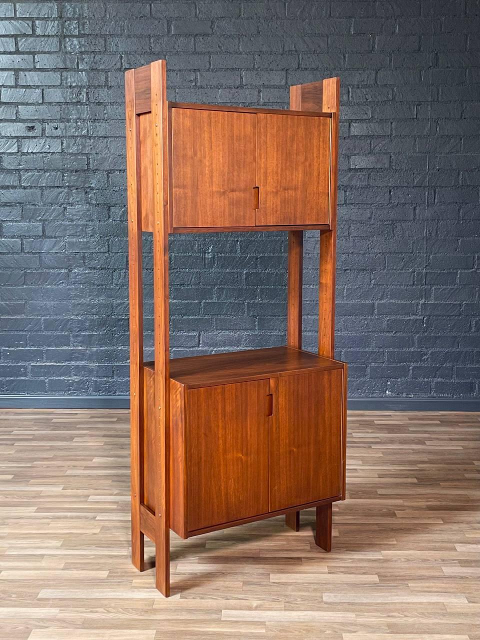 Condition: Original Vintage Condition 

This Mid-Century Modern free-standing bookshelf and storage unit features a clean architectural frame crafted in richly grained walnut. The design showcases two cabinet compartments—one upper and one