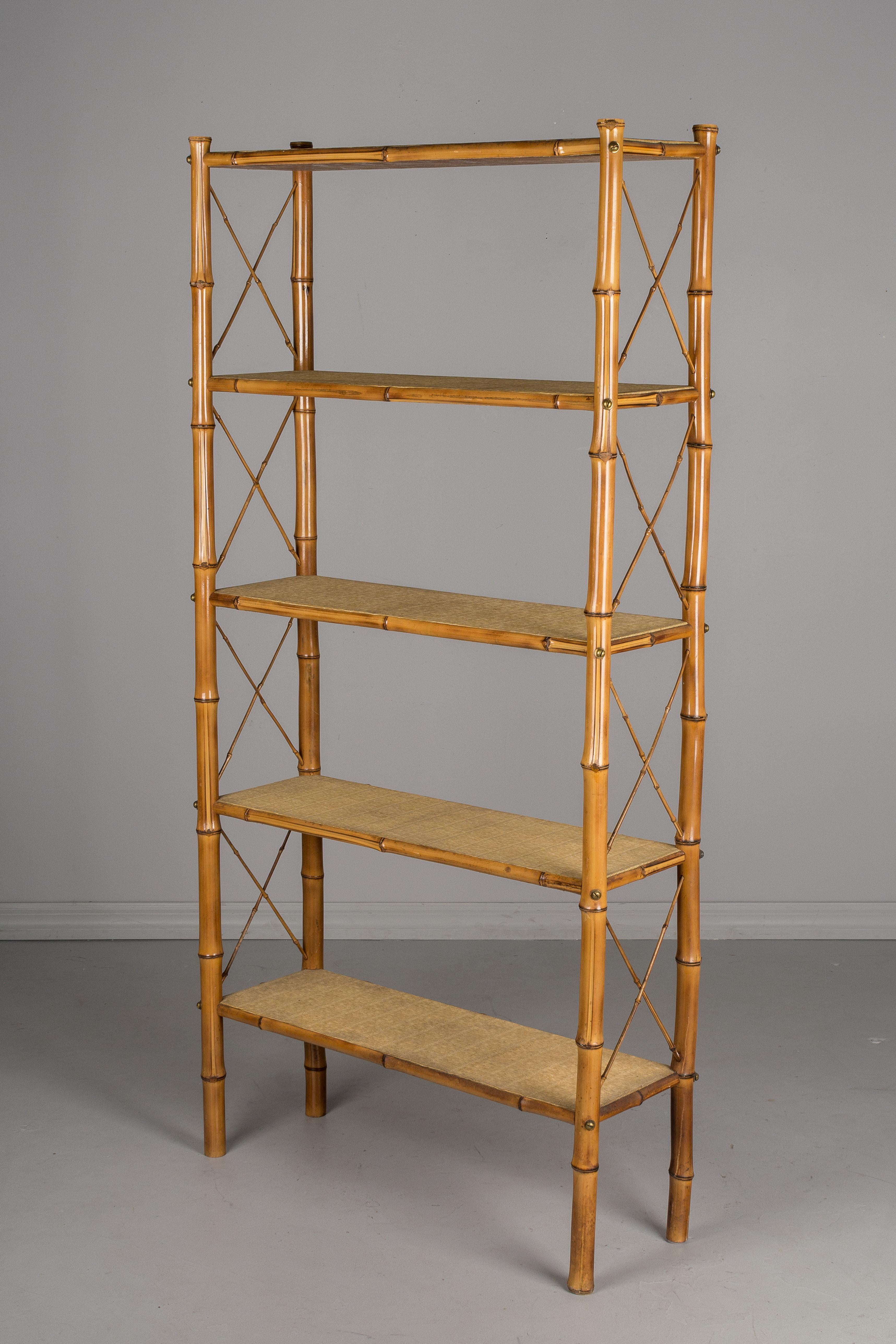 A Mid-Century Modern French étagère, or open bookcase, with a sturdy bamboo frame and tightly woven rattan shelves. Decorative X-supports on the sides. Shelves secured with brass screws. Four shelves are spaced 13