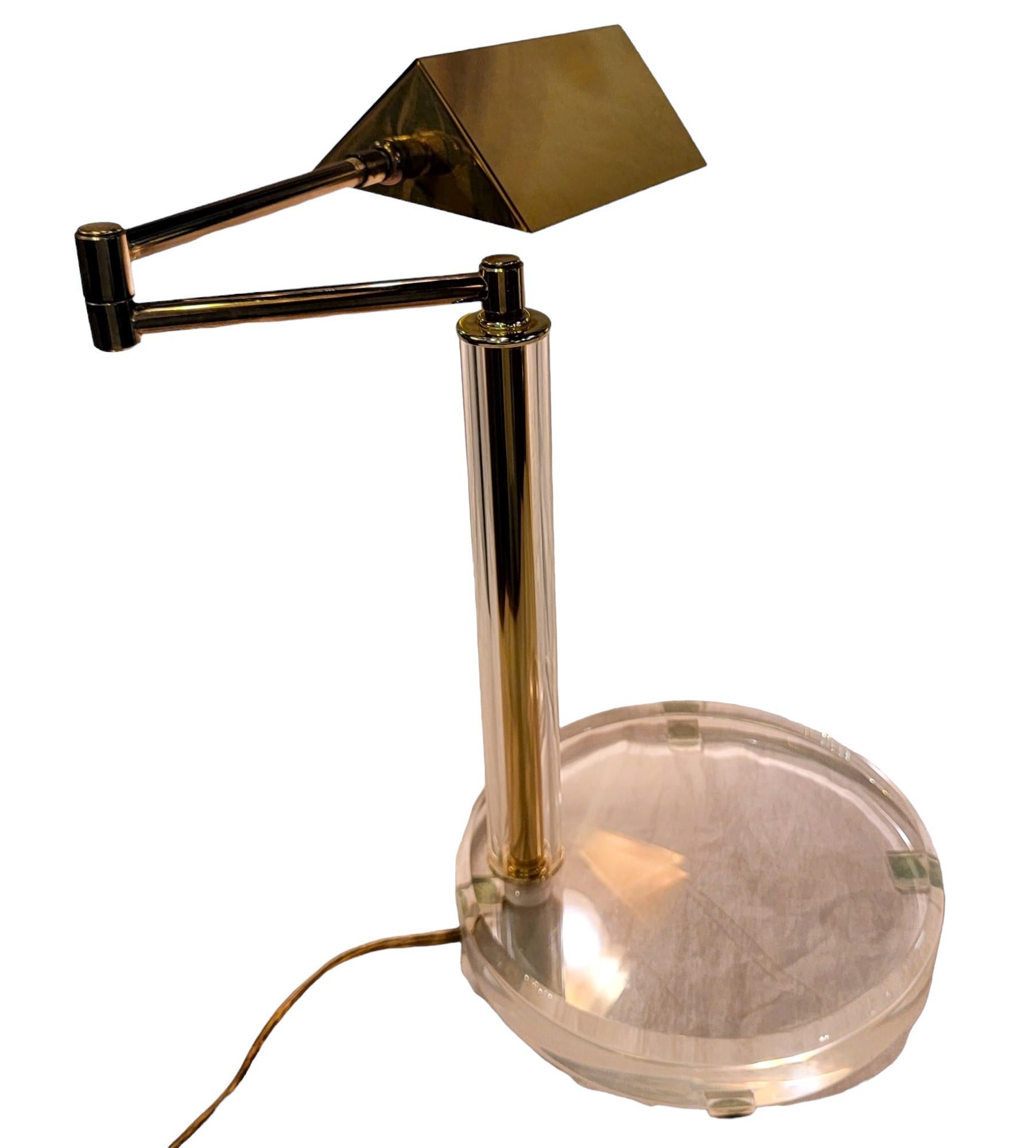 Mid Century Modern Walter Von Nessen French Brass and Lucite Table Lamp. The Lucite base extends upward and fully engulfs the brass stem.  There are minor scratches to the Lucite. The arm extends outward. 
Brass lamp - base 10 diameter.
Full Height