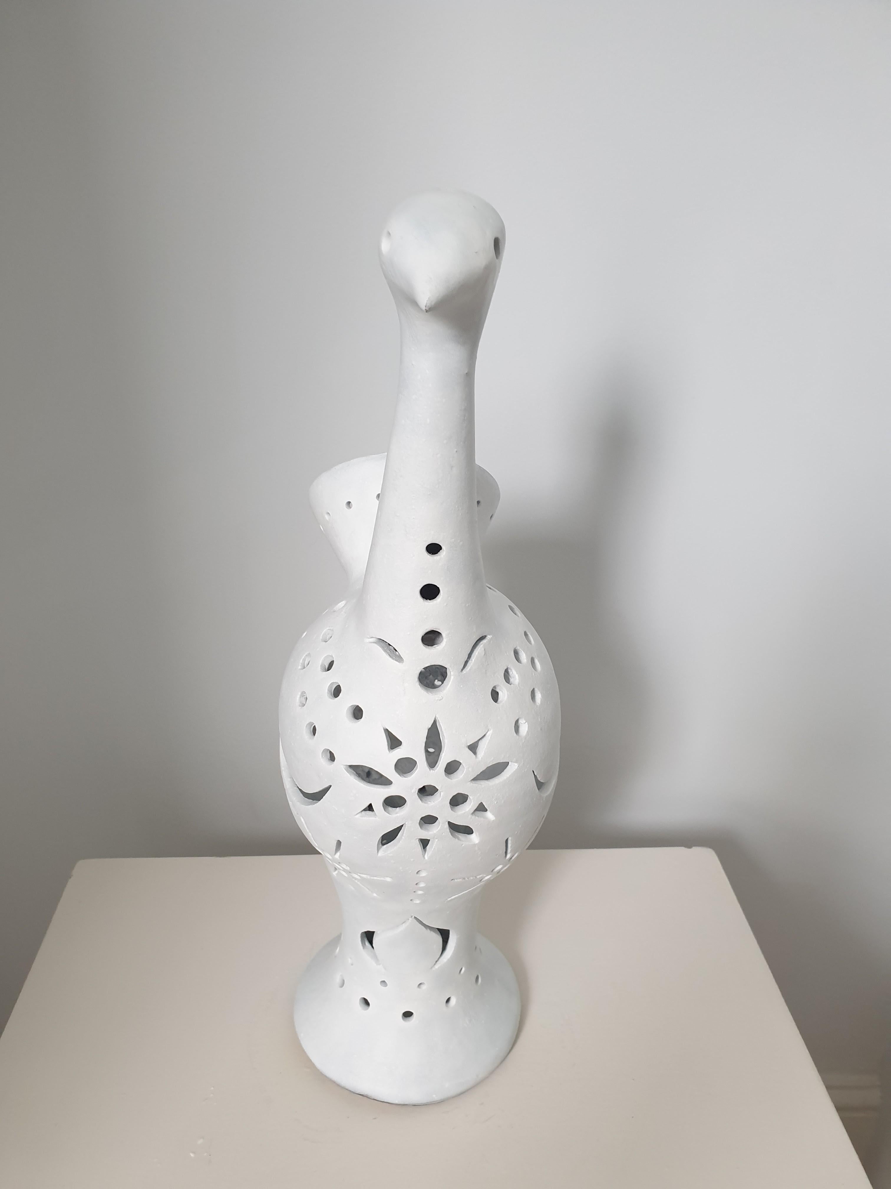 Large and imposing French white matt glazed ceramic lamp representing a stylized peacock. The lamp is unusual in that the lamp holder is inside and the light streams out via the perforations in the surface of the bird. The lamp will be rewired by
