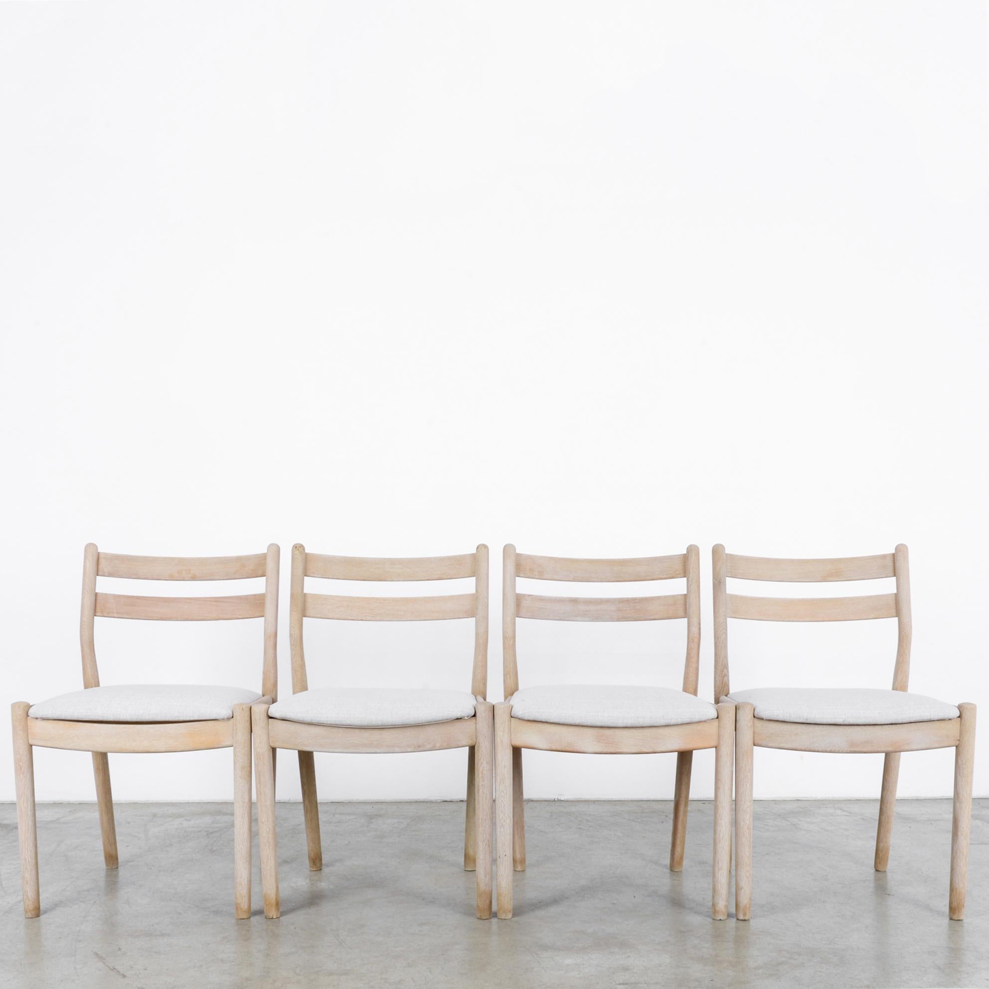 This set of four wooden chairs was made in France, circa 1960. Stone gray upholstered seats complement the pale tones and beautiful wood grain of the oak. The tilt of the backrests and the curves of the back rails and apron give these dining chairs
