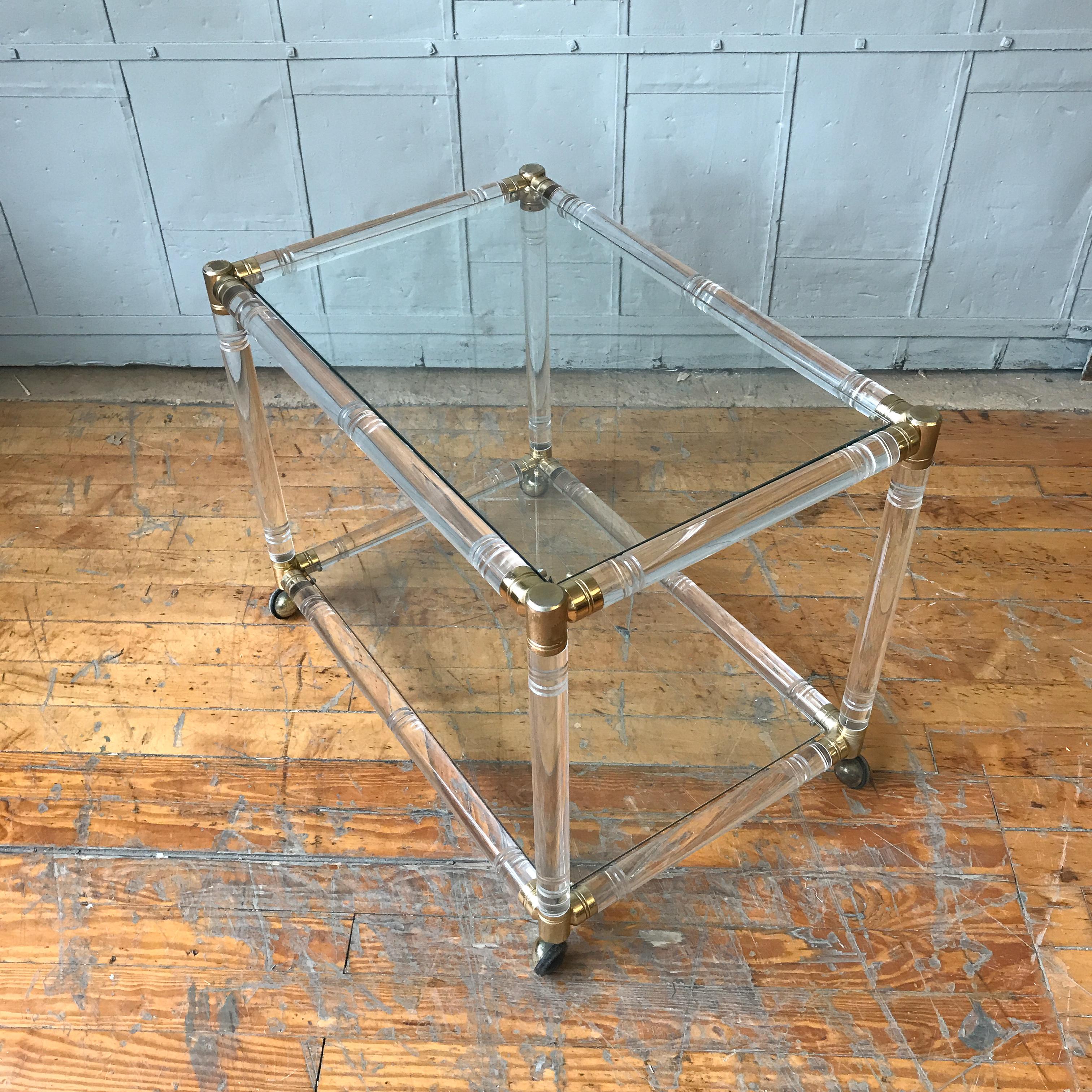 Ajoutez une touche de style moderne et de sophistication à n'importe quelle pièce avec ce superbe chariot de bar en plexiglas de style moderne français du milieu du siècle. Fabriquées en plexiglas avec des garnitures en laiton, les deux étagères en