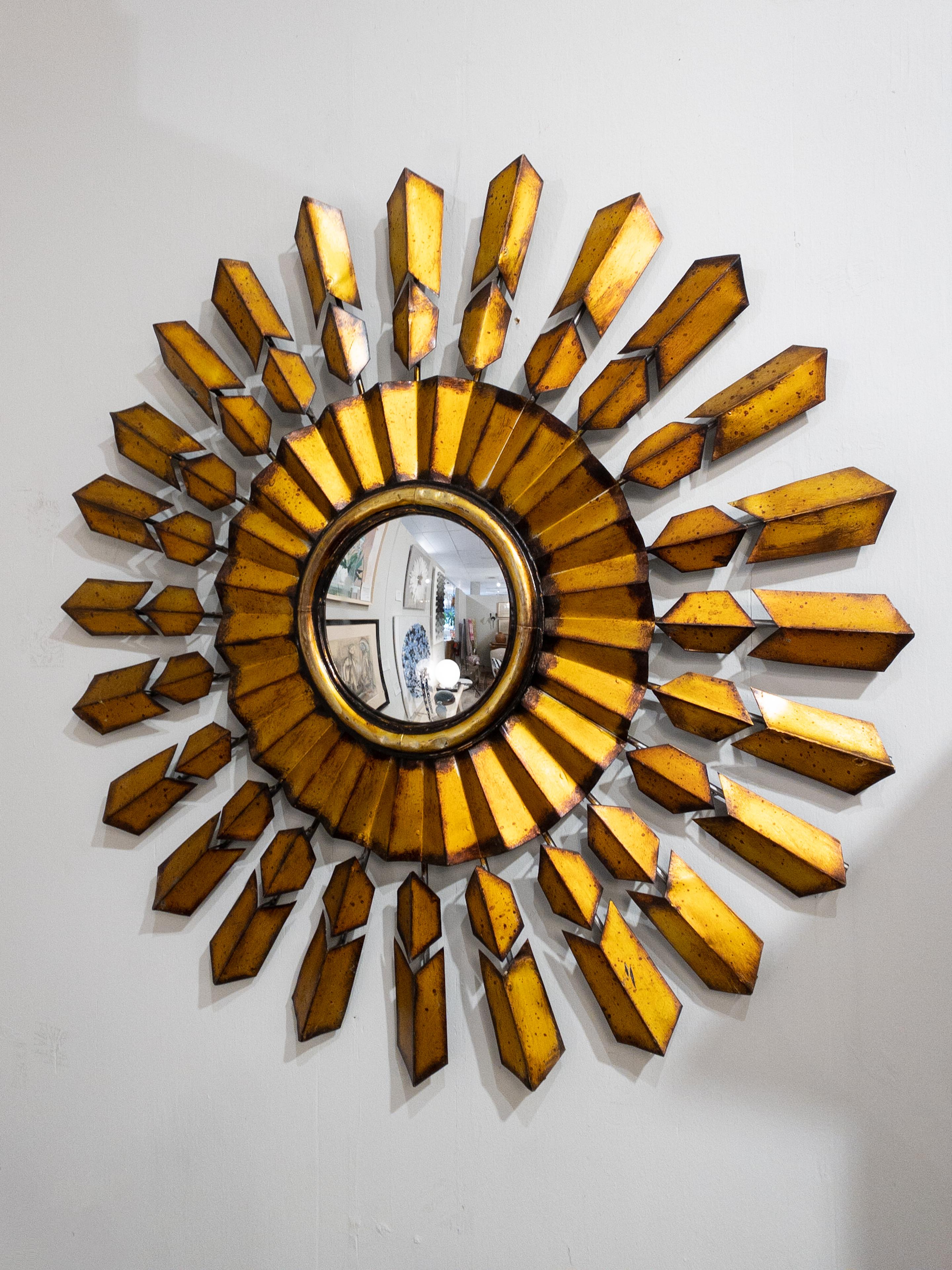 The Mid Century Modern French Sun Burst Mirror is a stunning and iconic piece of decor that captures the essence of the mid-century design era. Crafted from gilded metal, its sunburst shape radiates with a sense of energy and optimism, emblematic of