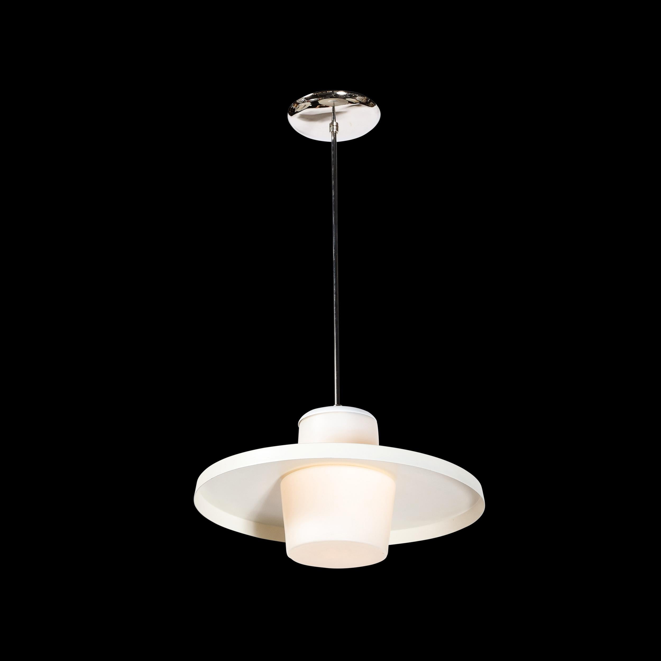 This refined and sophisticated Mid-Century Modern pendant was realized in Czechoslovakia circa 1950. Resembling a stylized flying saucer, the pendant features a white enamel tented shade with a raised lip that bisects the cylindrical frosted glass