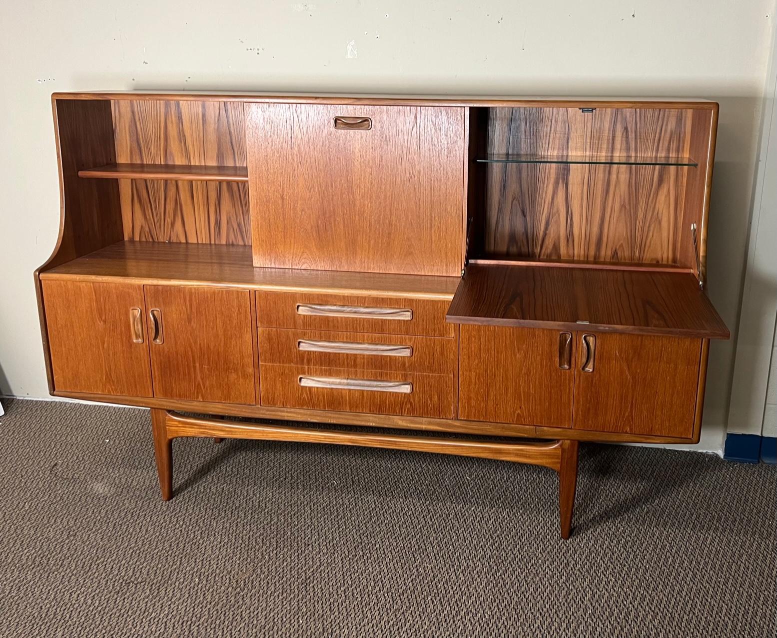 Mid-Century Modern versatile high board by G Plan. Featuring a sliding door and a small drop down desk that can comfortably hold a laptop or be used as a wine bar. Shelves are adjustable. Unfinished back.

Very good condition overall. All drawers