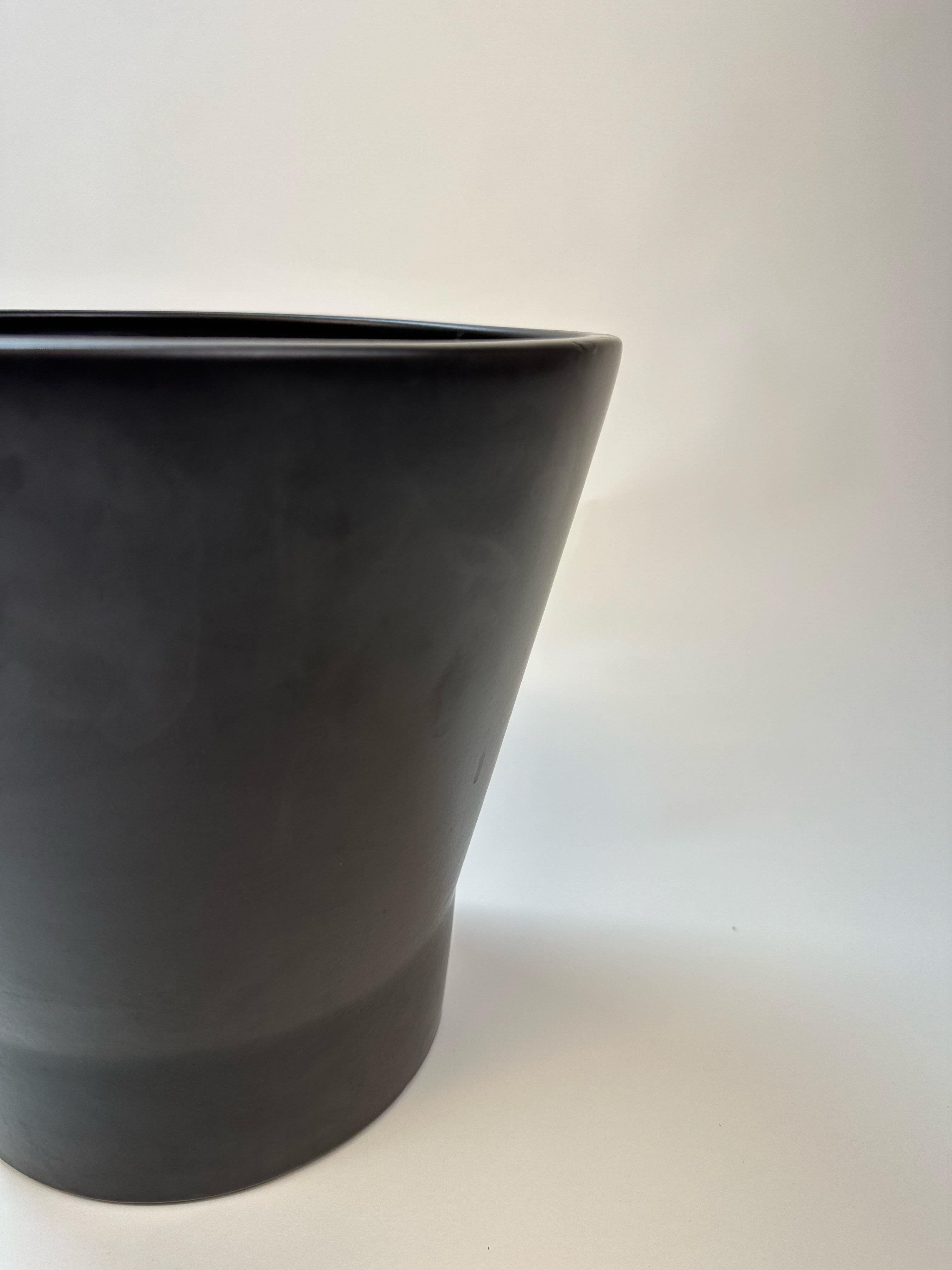 Exemple frappant du design californien intemporel, cette jardinière Gainey Ceramics du milieu du siècle présente une forme épurée et sculpturale avec une silhouette subtilement effilée. Finie dans un élégant glaçage noir mat, la pièce offre une