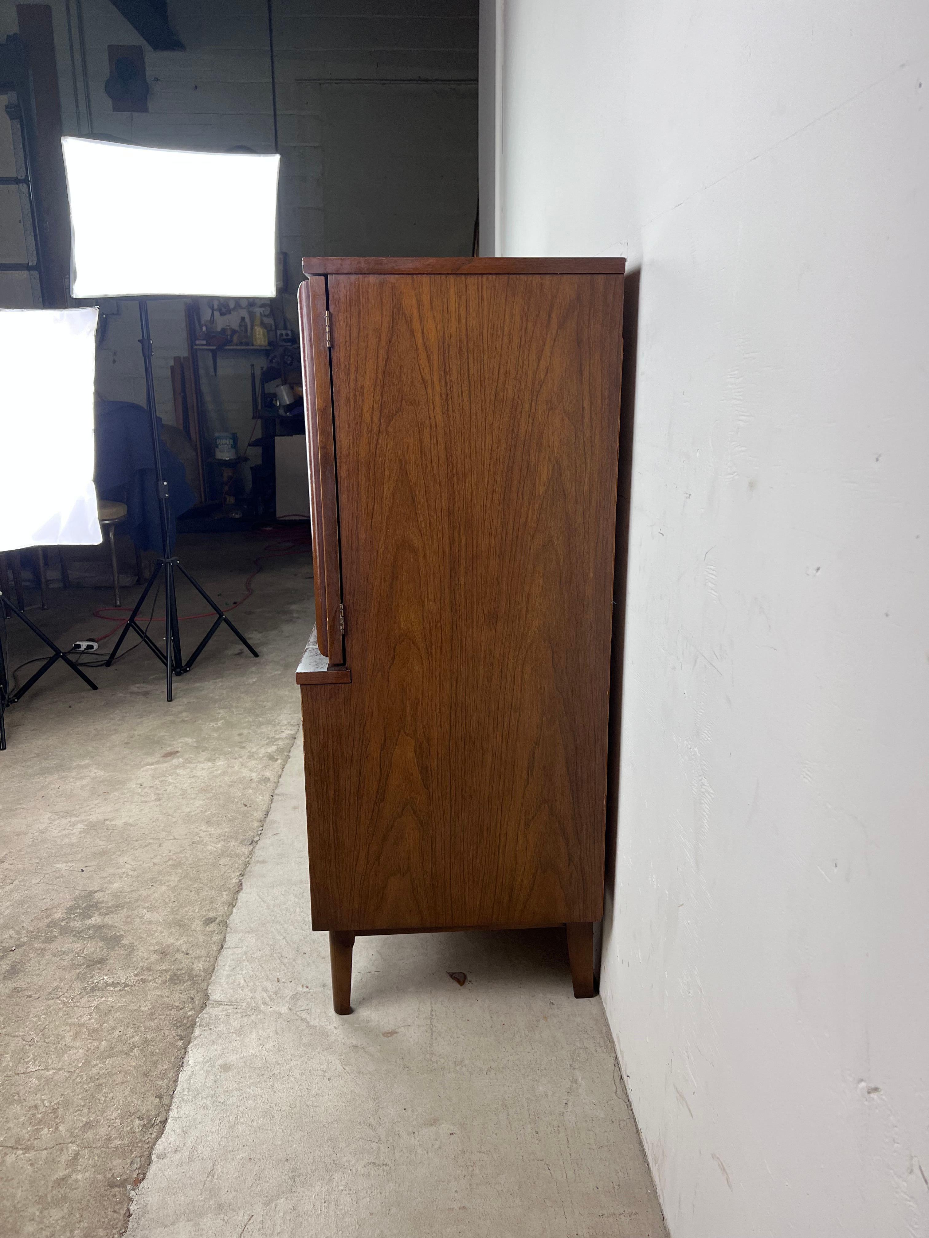 This Mid-Century Modern gentleman's chest features hardwood construction, walnut veneer with original finish, five dovetailed drawers with brass accented hardware, two cabinet doors with sculpted wood pulls, and tall tapered legs. ??

Matching