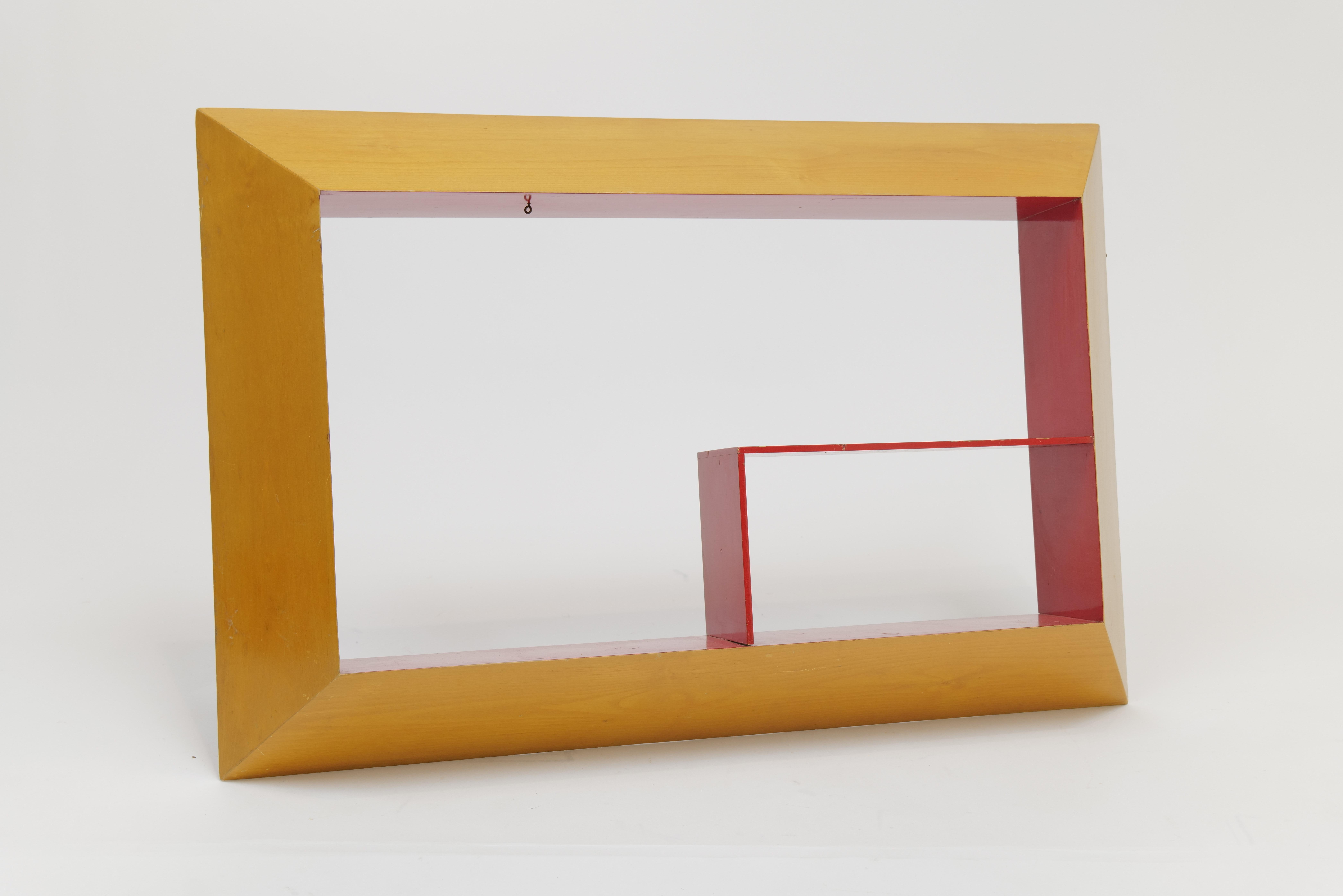 A dynamic and graphic Mid-Century Modern shadow box wall shelf, featuring an asymmetrical geometric composition and bold color contrast. The outer frame is finished in a warm blonde wood tone, while the interior shelving and inner frame pop in a