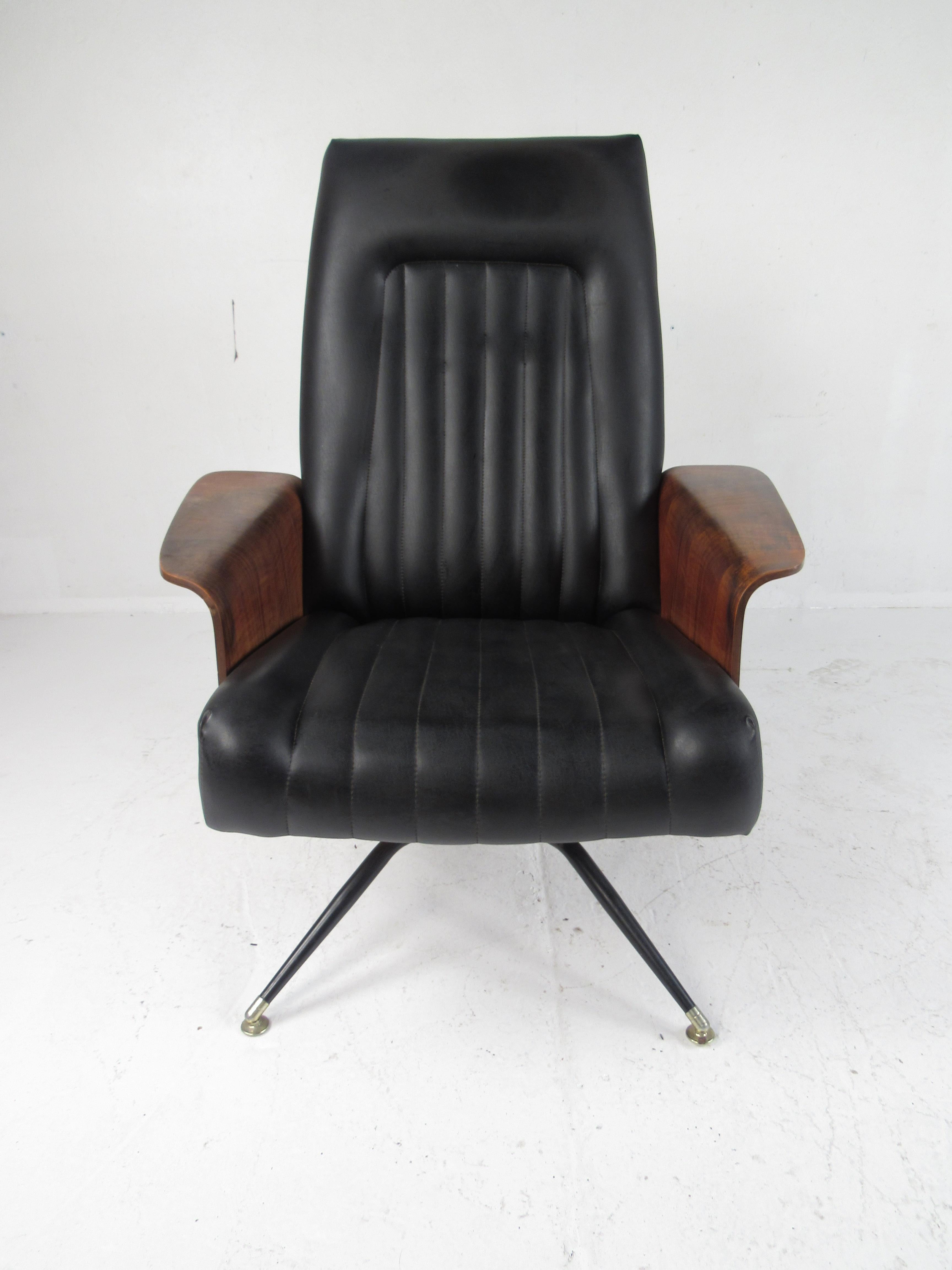 A stunning 1960s lounge chair by Murphy Miller. This gently used swivel lounge chair boasts winged walnut armrests and vinyl upholstery. A vintage gem that has an unusual swivel metal base with splayed legs. An iconic design in the style of George