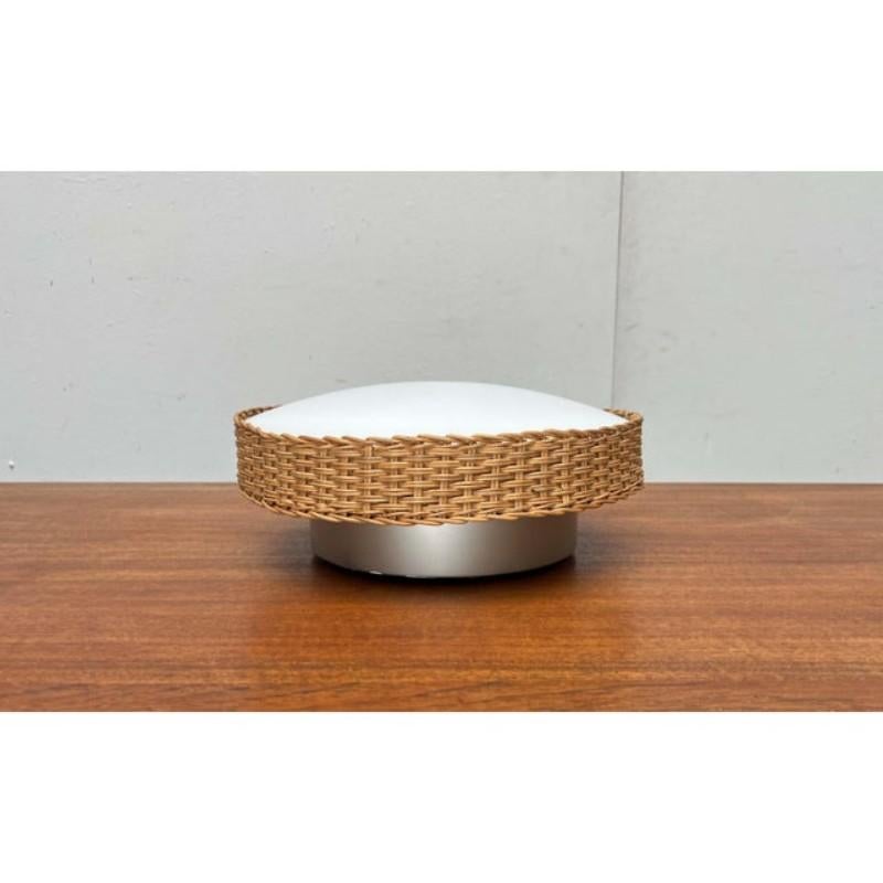 A mid-century ceiling light by Kaiser Leuchten featuring a distinctive material.

The light consists of a base with a socket, a round opal glass diffuser, and a drum-shaped shade. The diffuser glass is framed by a wickerwork shade. The light is set