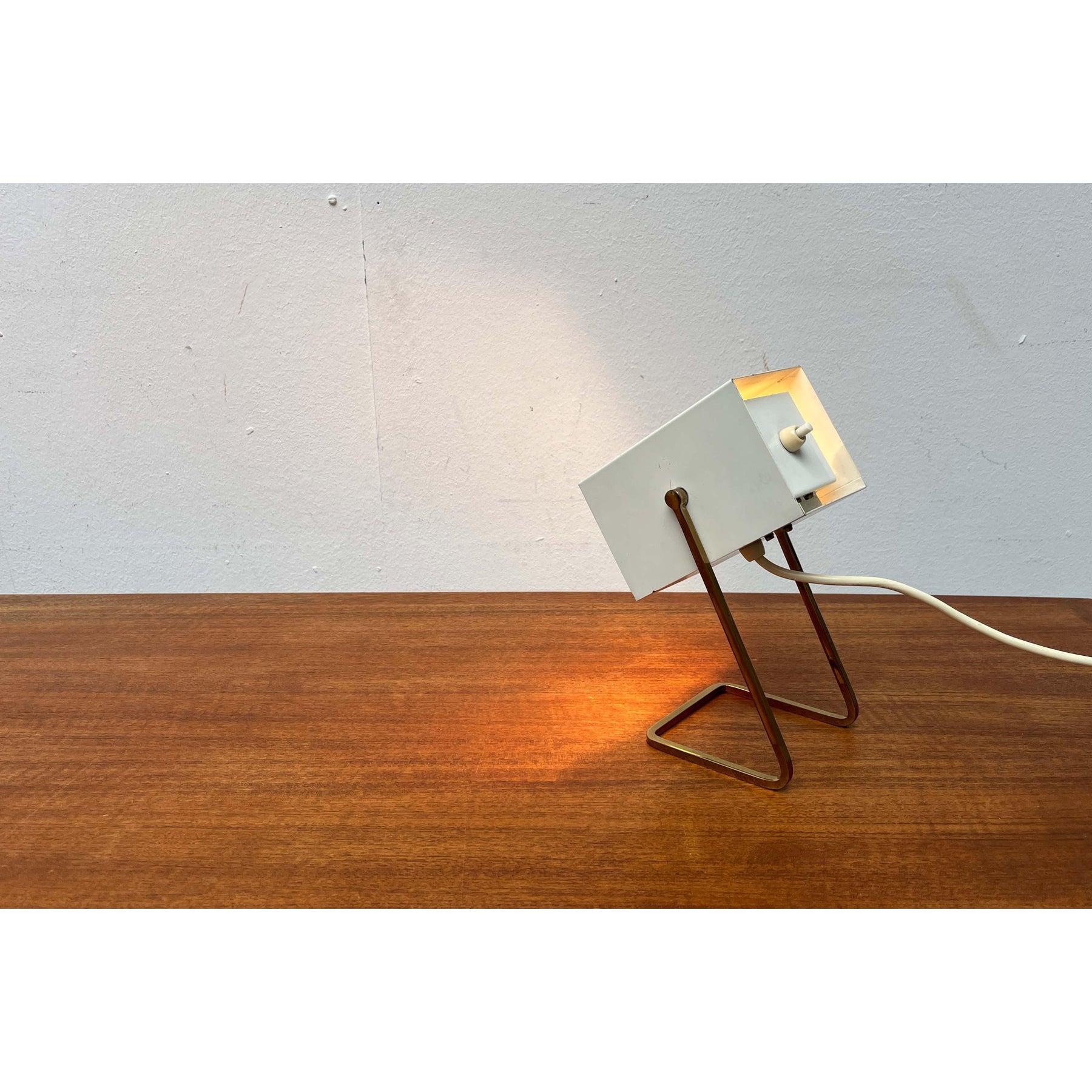 Pequeña lámpara de sobremesa de Kaiser Leuchten.

Un diseño minimalista con forma cúbica. La sencilla cabeza de la lámpara está abierta por un lado y pivota, lo que permite inclinarla hacia arriba y hacia abajo. La base está dividida en un delicado