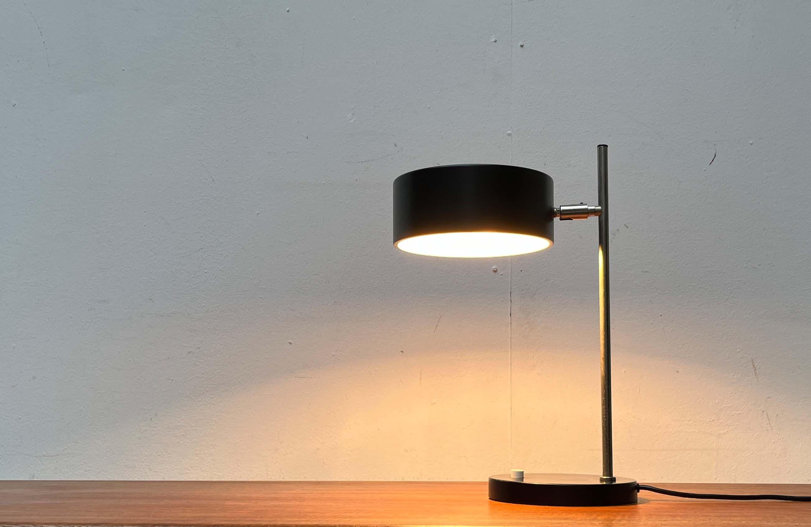Rare lampe de table du milieu du siècle dernier. Probablement du Kaiser Leuchten.

Un design minimaliste. L'abat-jour rond et plat en métal est fini en noir. La couleur est répétée dans le capuchon du pied. L'écran est relié à l'arbre par une