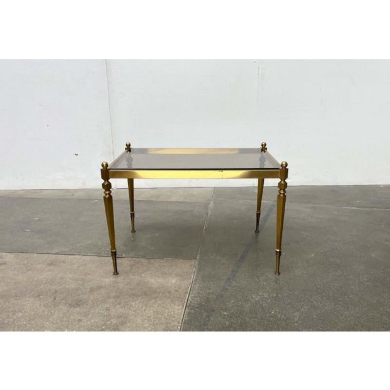 Tavolino di metà secolo in stile neoclassico.

Il tavolo è costituito da una struttura in ottone con un piano in vetro fumé. La solida struttura forma un'ampia cornice rettangolare nella parte superiore, che racchiude il piano del tavolo. Le gambe