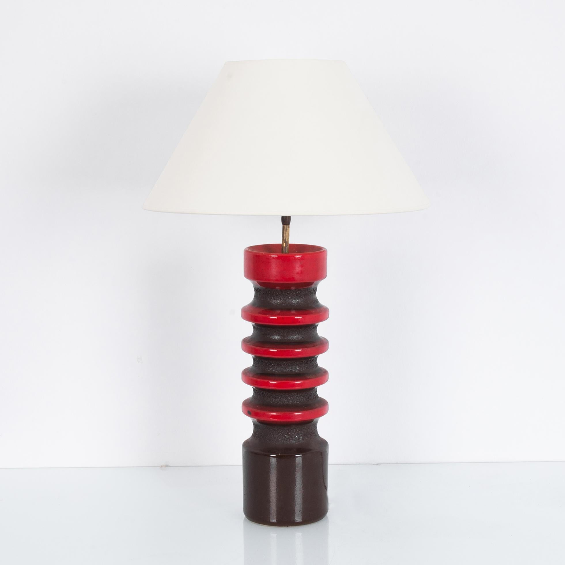 A ceramic table lamp from Germany, circa 1960. Punchy color and intriguing shape; a black and red ceramic column supports a simple lampshade in natural white. The ribbed silhouette is amplified by the cherry red enamel which alternates with a dark