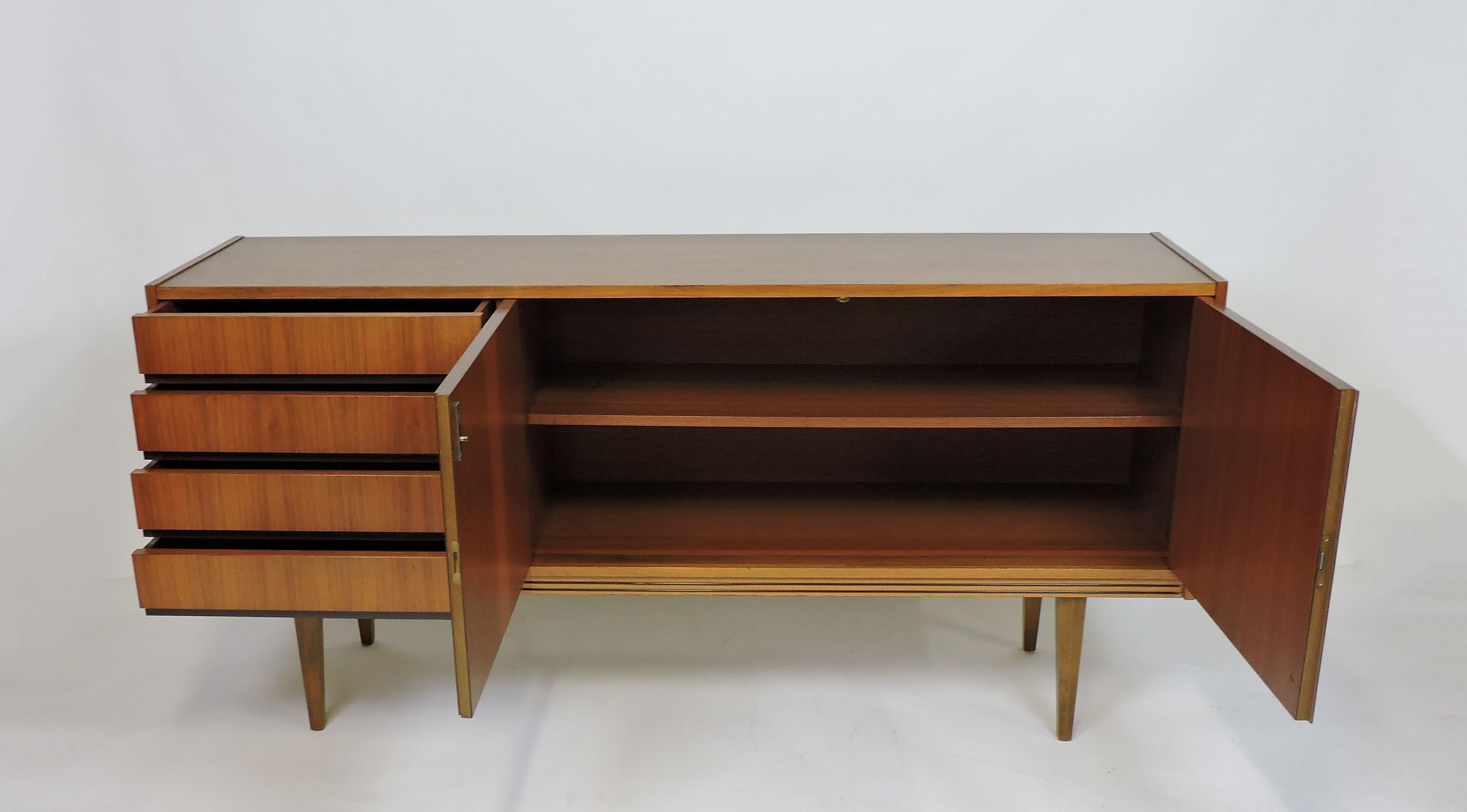 Handsome and well made midcentury teak cabinet made in Germany by Munker Modell. This credenza has four drawers, two doors that lock, an interior shelf, and tapered legs. The top drawer has a felt lining and there is a label on the back. A key is