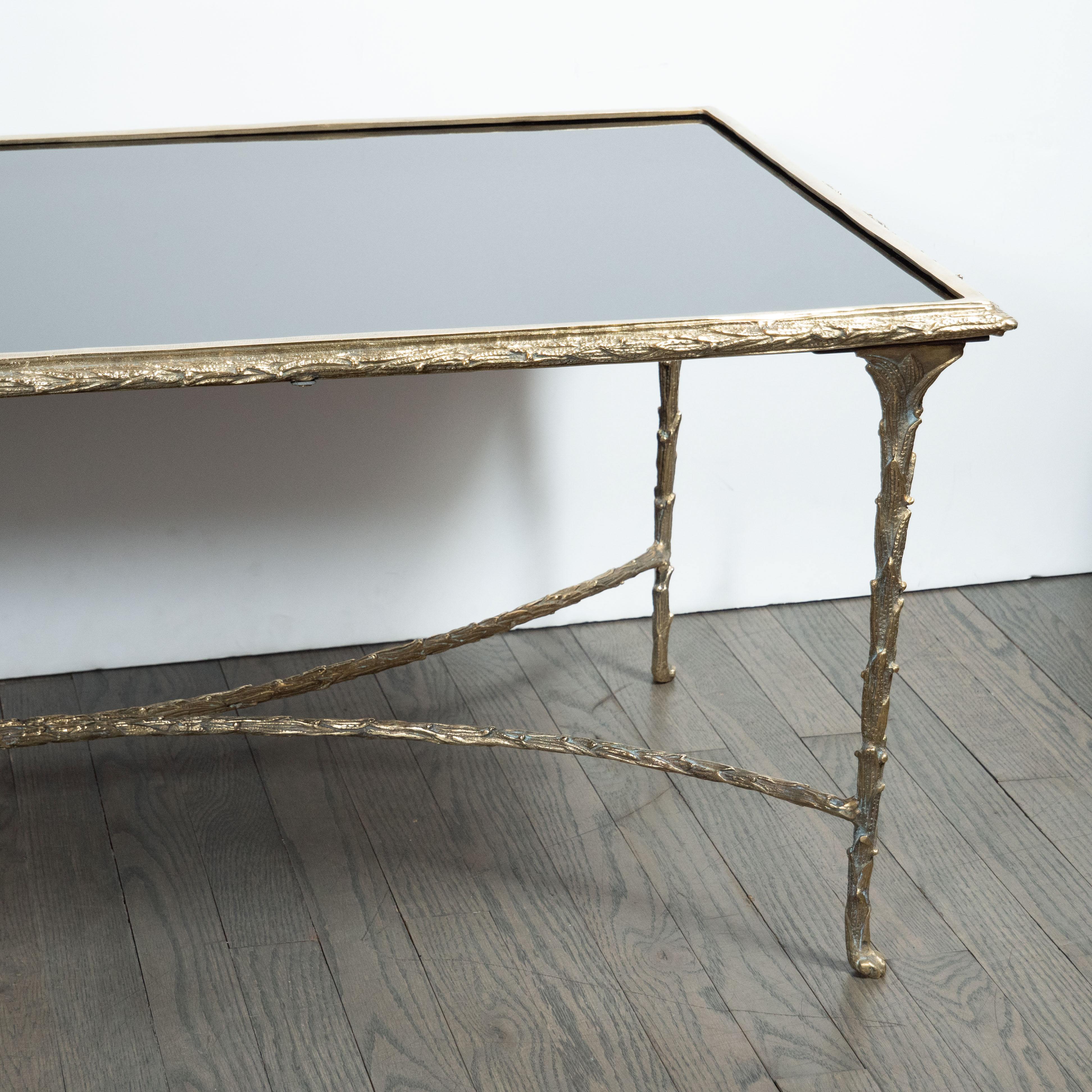 This elegant Mid-Century Modern cocktail table was realized by the esteemed French maker Bagues, circa 1950. It features a rectangular black vitrolite top sitting in a gilded bronze frame with dappled and sculptural foliate detailing engraved