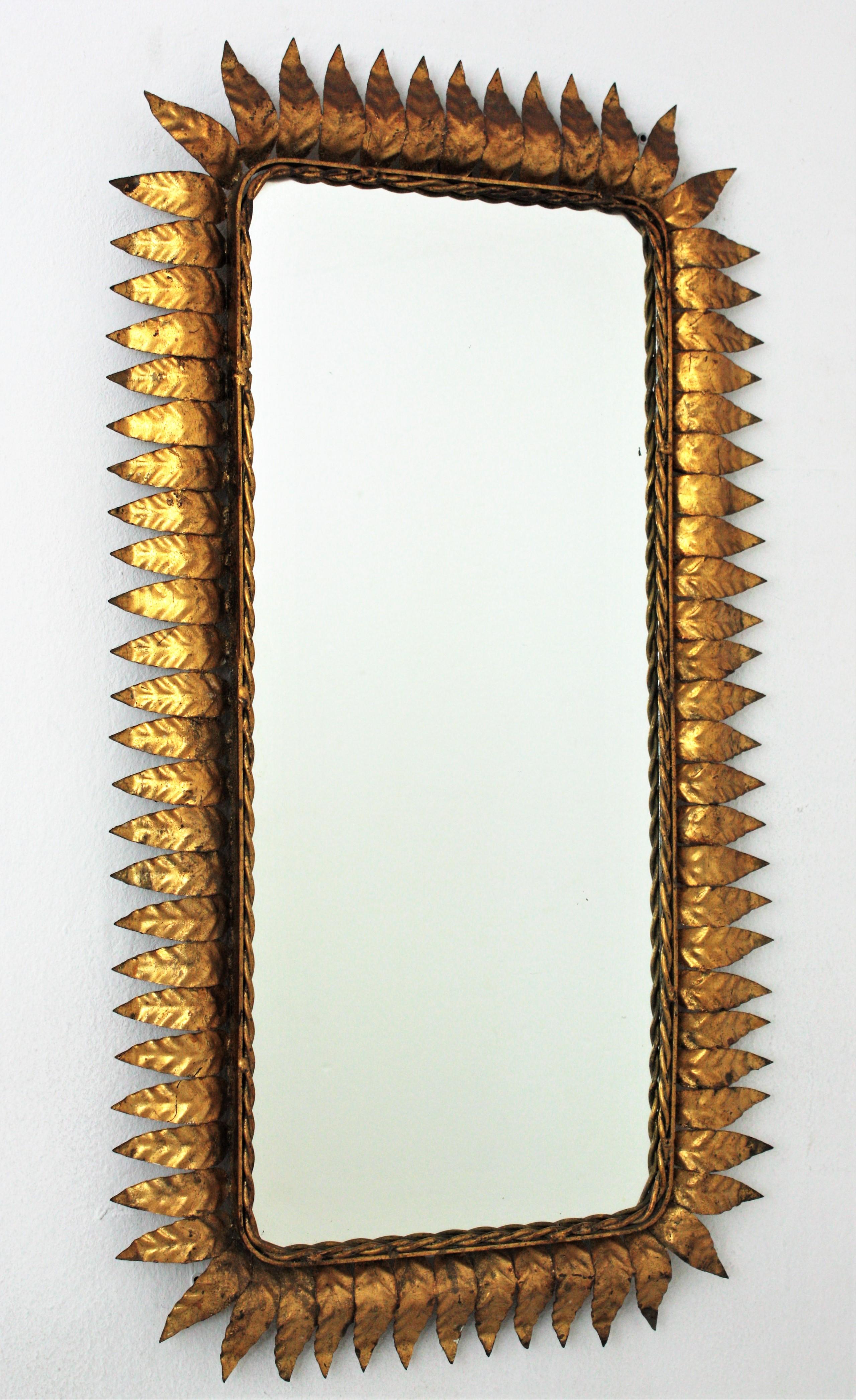 Hand-hammered iron sunburst rectangular wall mirror with gold leaf finish, Spain, 1950s.
Its highly decorative rectangular leafed frame with gold leaf gilding and its large glass surface makes this piece very interesting. 
A great choice placed in
